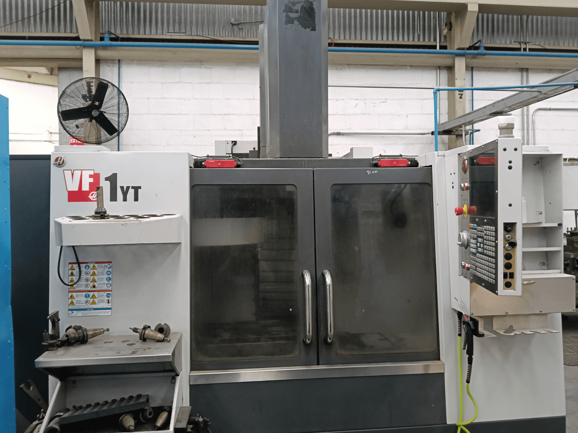 Вигляд спереду вертикального обробного центру HAAS VF-1YT-1 з панеллю керування та інструментами збоку.