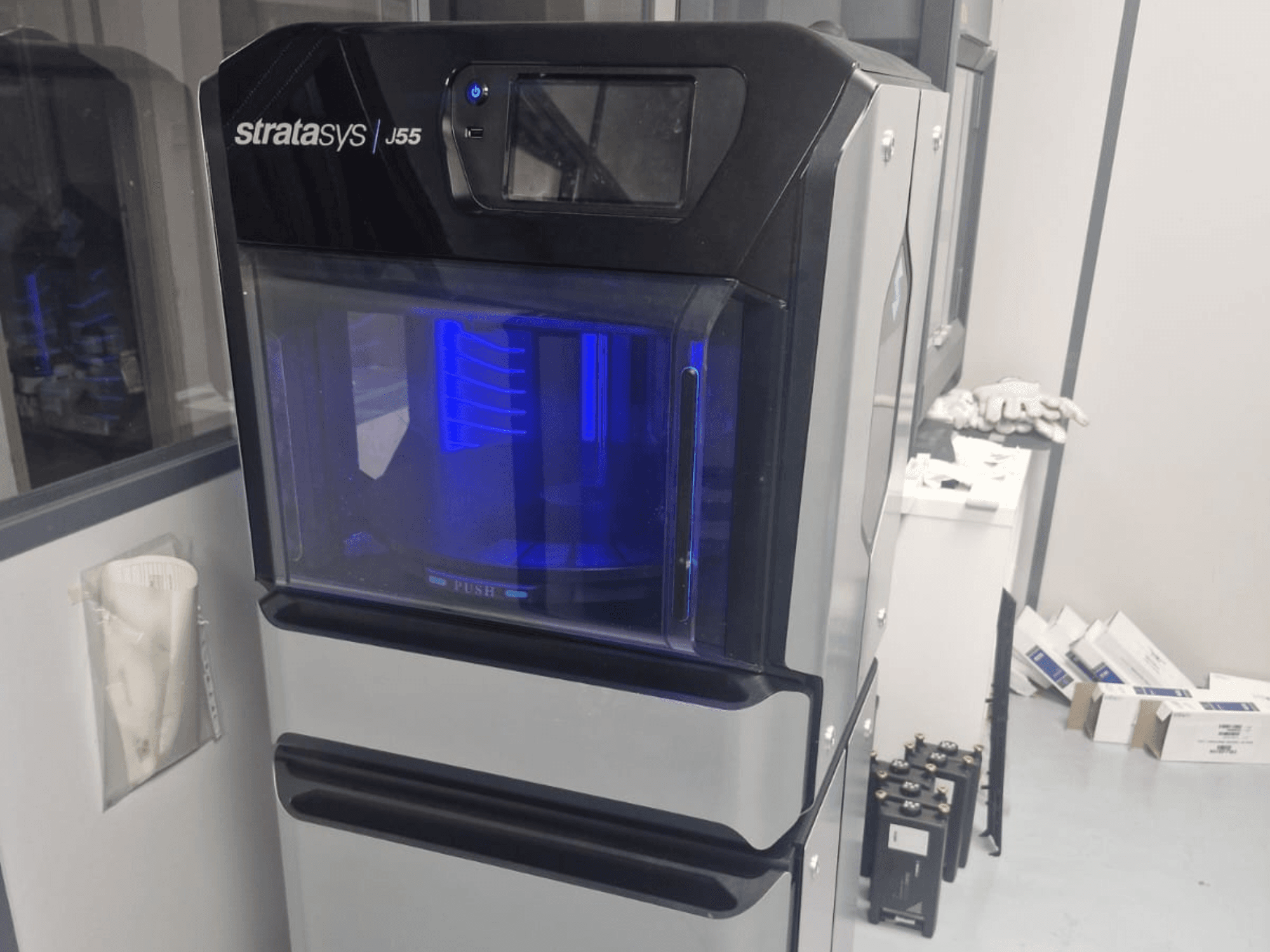 Пластиковий 3D-принтер Stratasys J55 Prime у вигляді збоку, що демонструє його витончений дизайн і підсвічування зони друку.