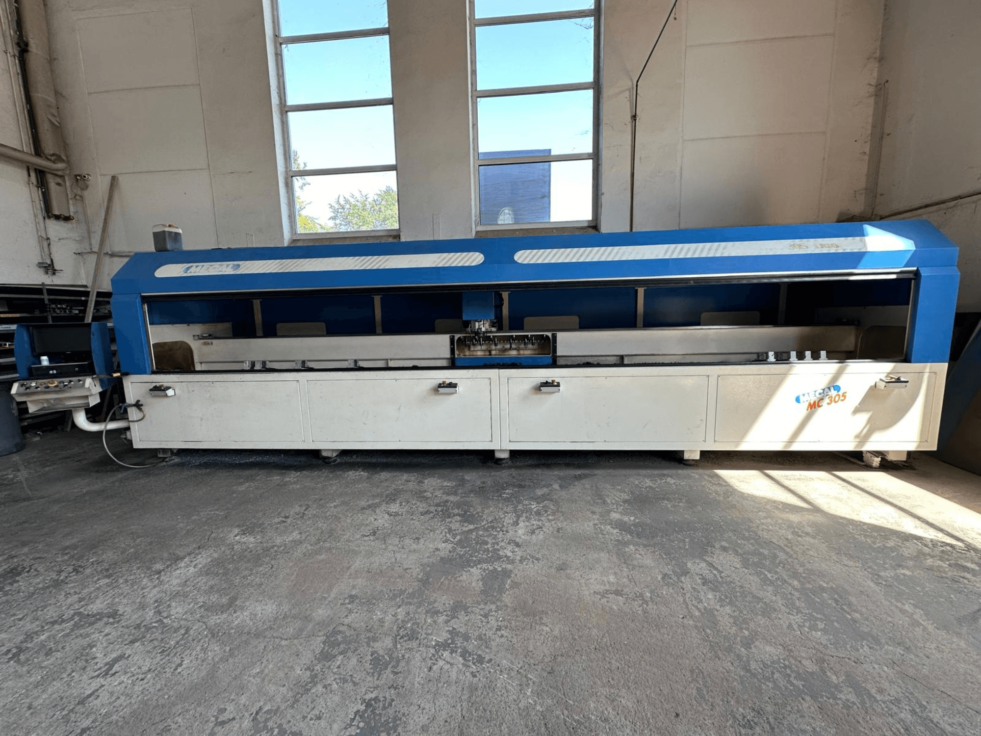 Вид спереду вертикального обробного центру MECAL MC 305 з синьо-білим дизайном, видимим робочим столом і панеллю керування.