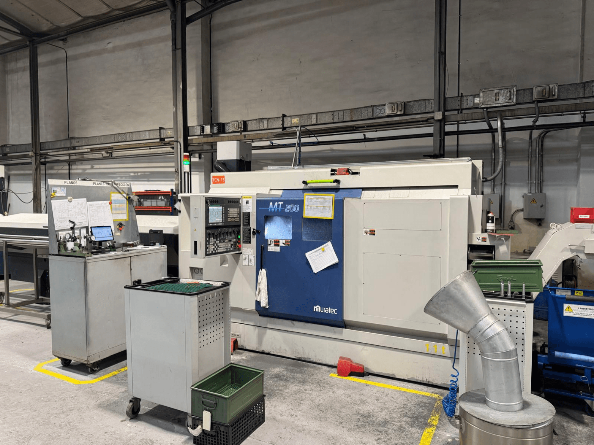 Багатошпиндельний токарний верстат Muratec MT200 у заводських умовах, вид спереду, з панеллю керування та навколишнім обладнанням.