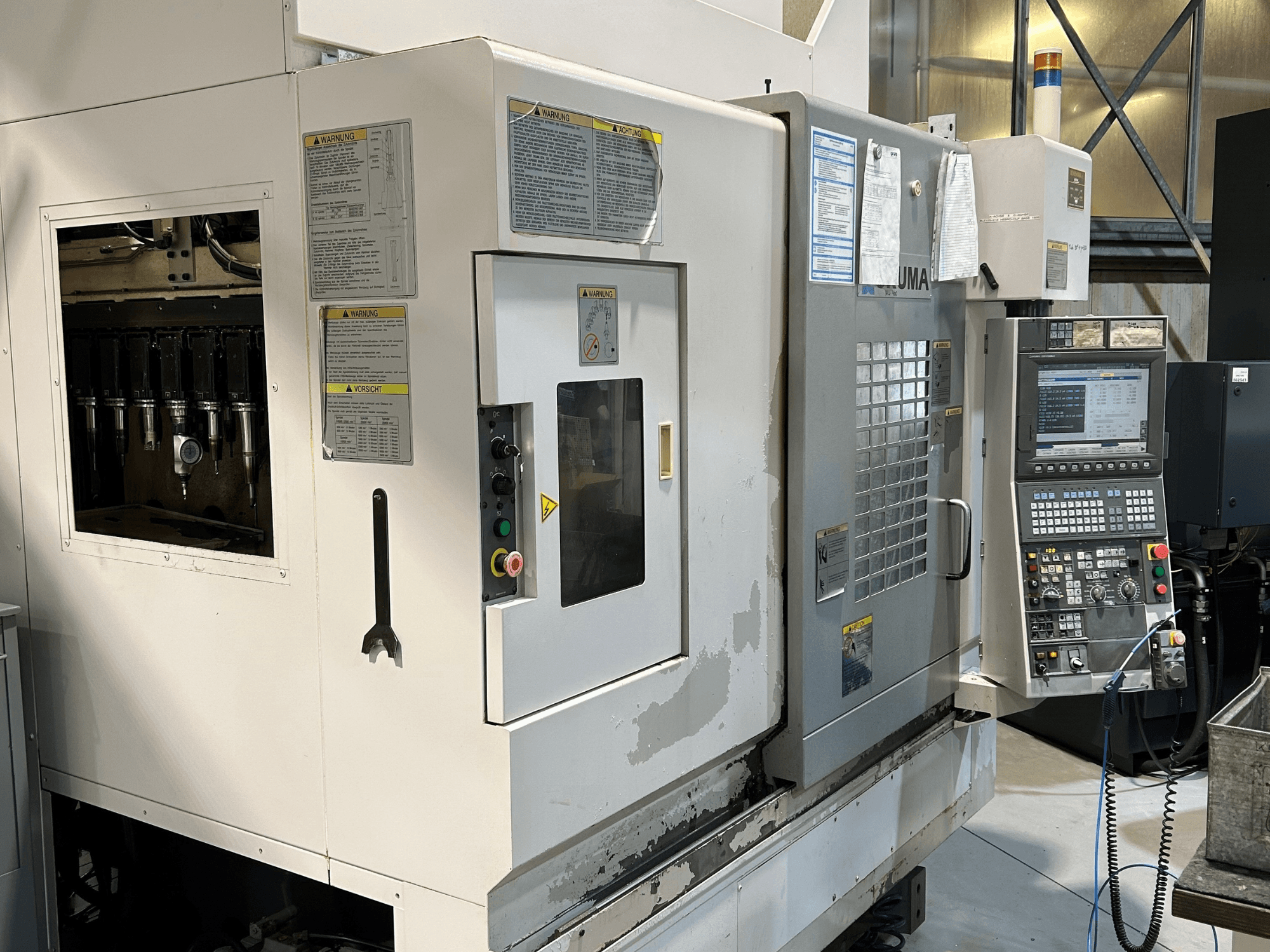 Вид спереду верстата з ЧПК UMA з видимими тримачами інструментів, панеллю керування, попереджувальними написами та кнопками керування.