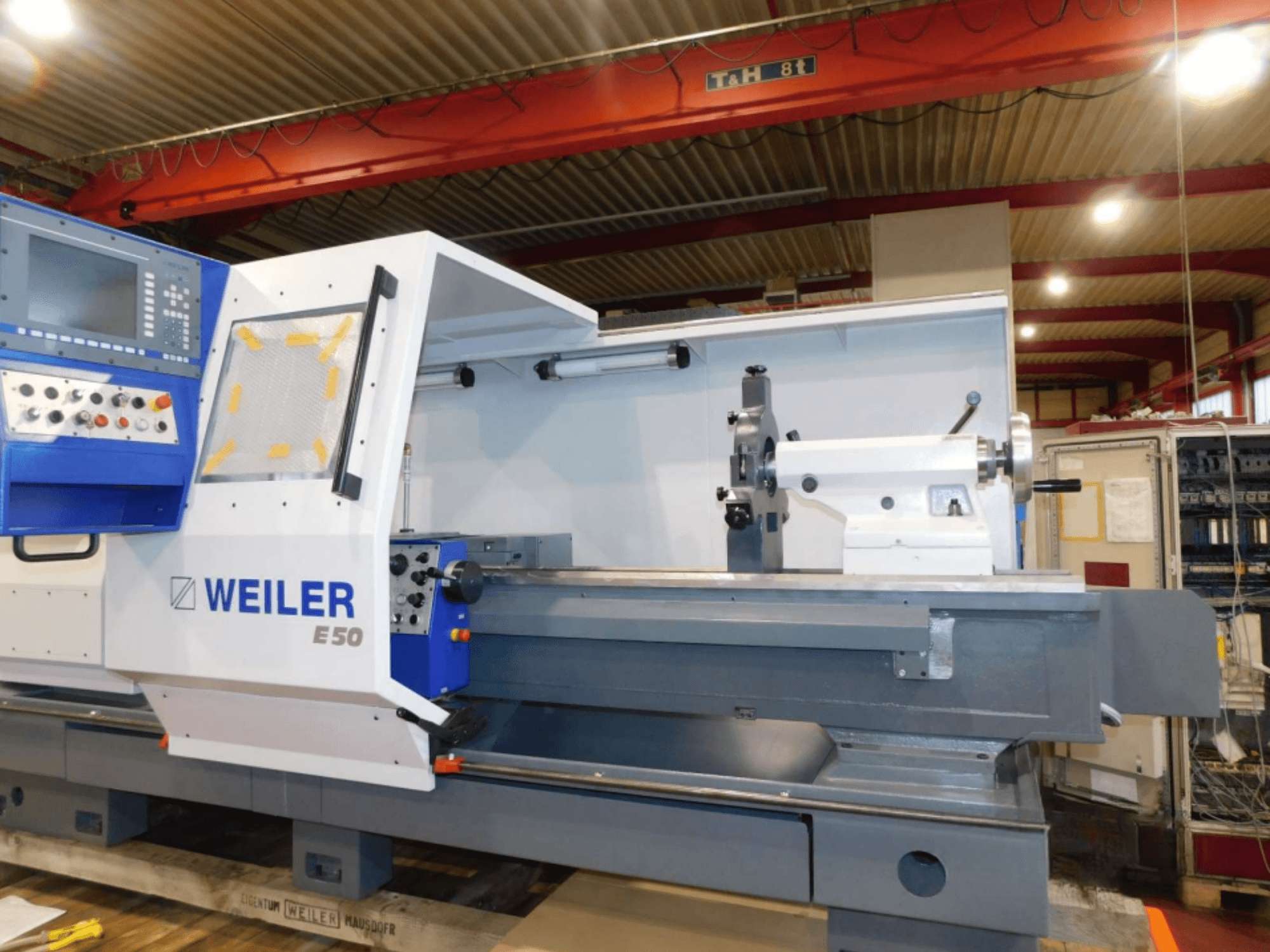 Горизонтальний токарний верстат Weiler E50, вид спереду, оснащений панеллю керування, шпинделем і прецизійною станиною з аксесуарами.