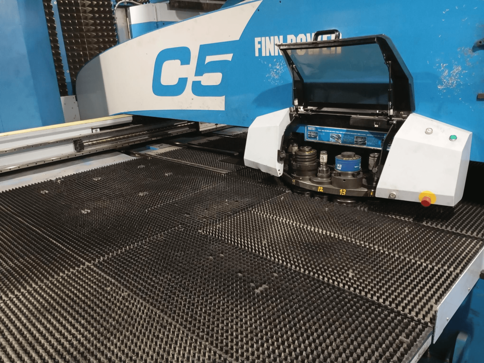 Пробивний прес Finn-Power C5, вид спереду, з відкритою головкою інструменту над текстурованим робочим столом з пронумерованими точками індексації.