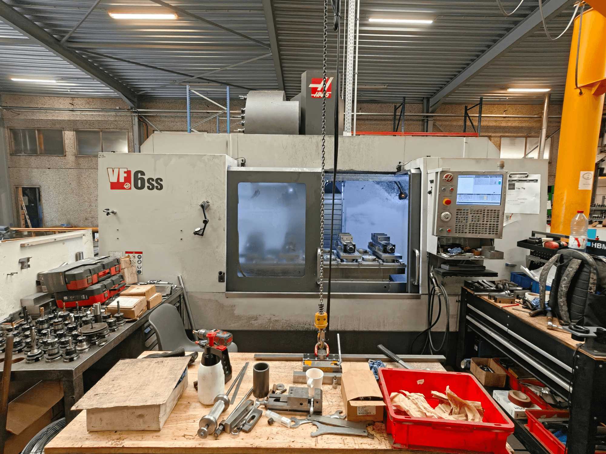 Вертикальний обробний центр Haas VF-6SS у цеху, вид збоку, на якому видно панель управління та робочу зону, захаращену інструментами.