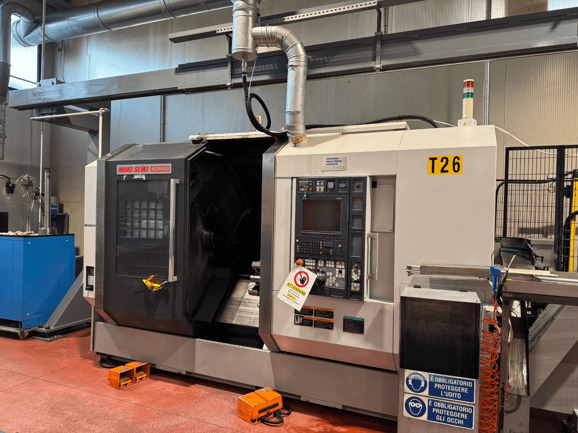 Токарно-фрезерний центр MORI SEIKI NZ-2000/T2/Y2, вигляд спереду, панель керування, знаки безпеки та промислове налаштування.