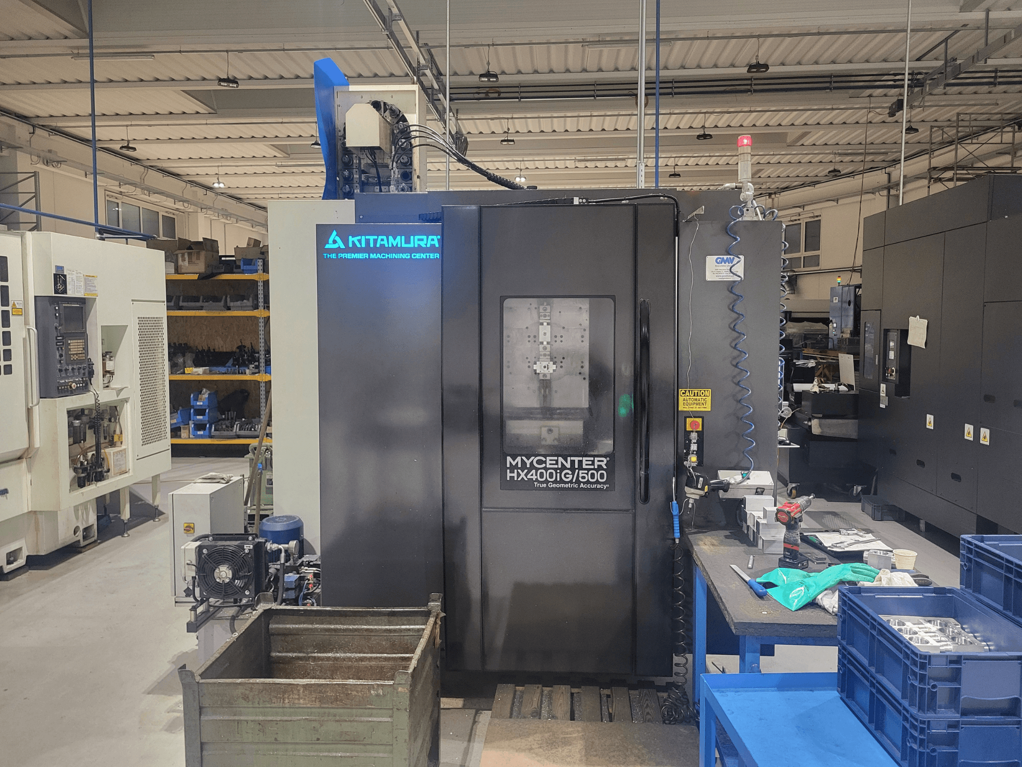 Верстат з ЧПК Kitamura Mycenter HX400iG/500 в майстерні, вид спереду, з елементами керування, сховищем для інструментів та матеріалів поруч.