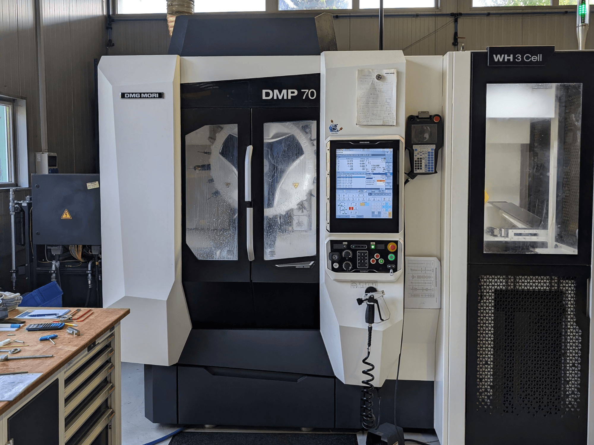 Вертикальний обробний центр DMG MORI DMP 70, вид спереду з панеллю керування та робочим дисплеєм, оточений верстатами цеху.