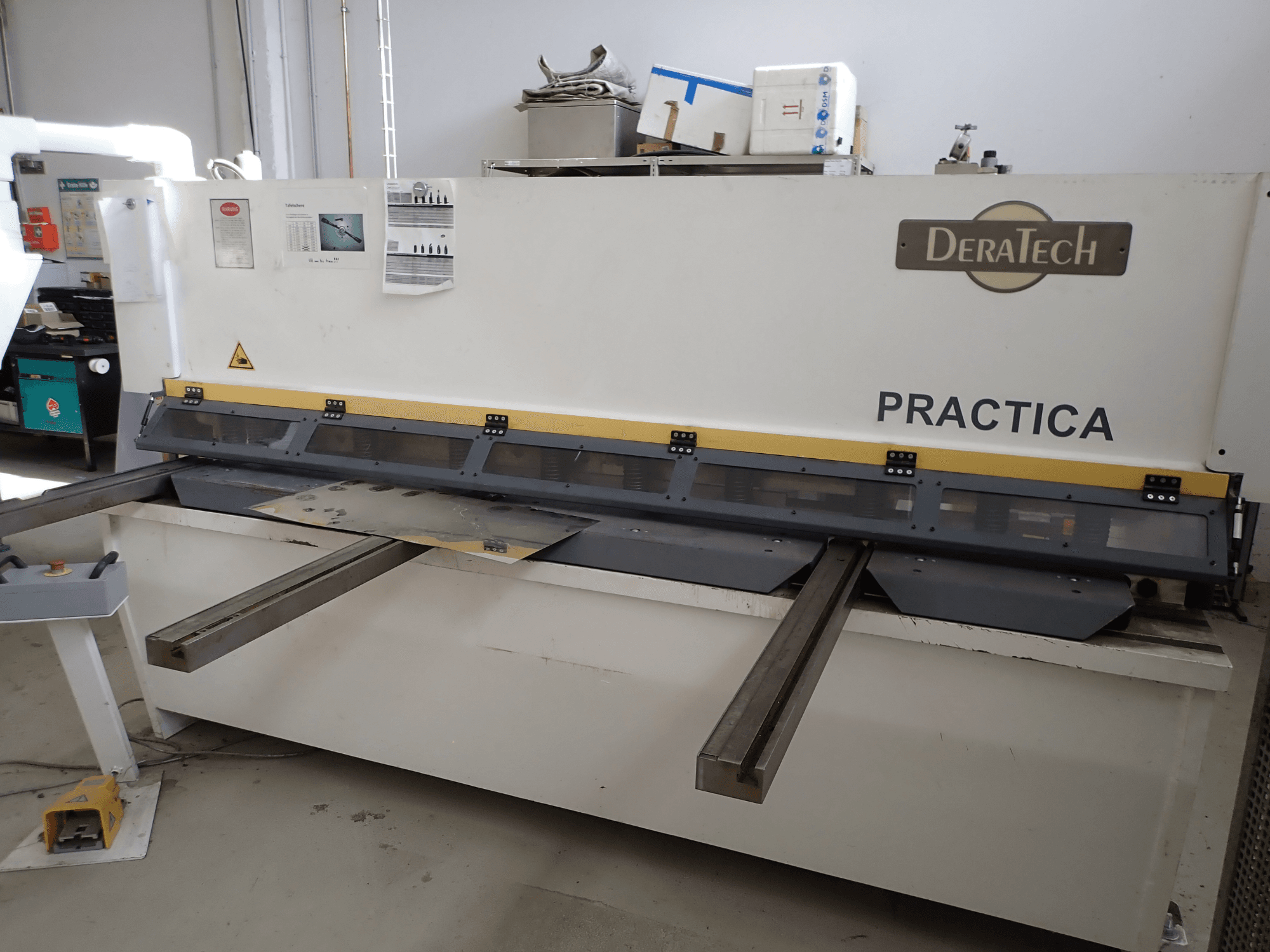 Відрізний верстат з ЧПУ DERATECH Practica, вид спереду, з ріжучим лезом і металевими листами на робочій поверхні.