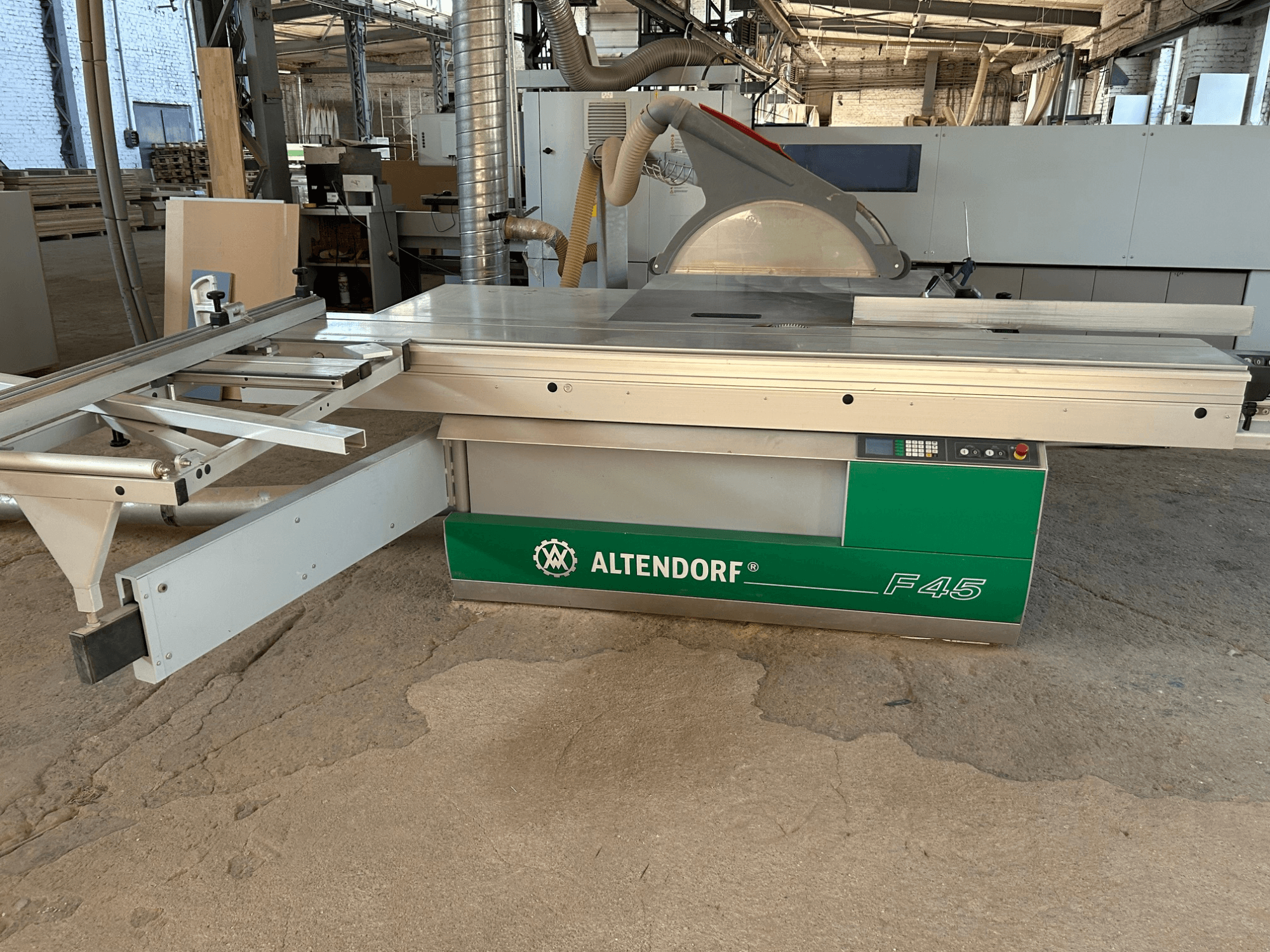 Пила для розпилювання плит Altendorf F 45, вид спереду, на якому видно робочий стіл, захисний кожух пильного диска та панель управління на машині зеленого та сірого кольорів.