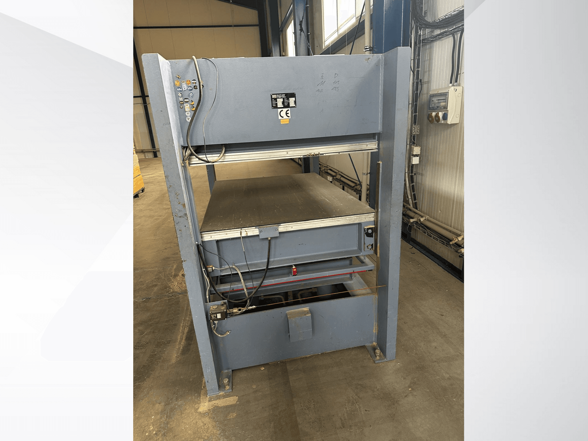 Сіра промислова машина з панеллю керування, вид спереду; включає регульовані платформи та знаки безпеки.