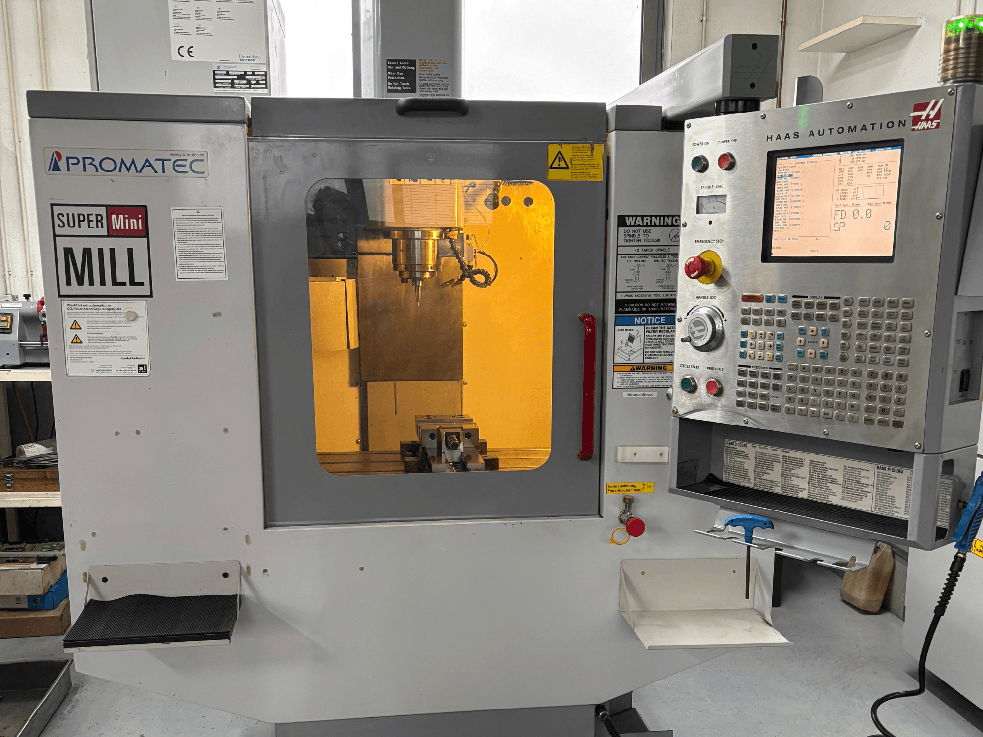 Фрезерний верстат Promatec Super Mini спереду, оснащений панеллю керування Haas Automation і видимим ріжучим інструментом всередині.