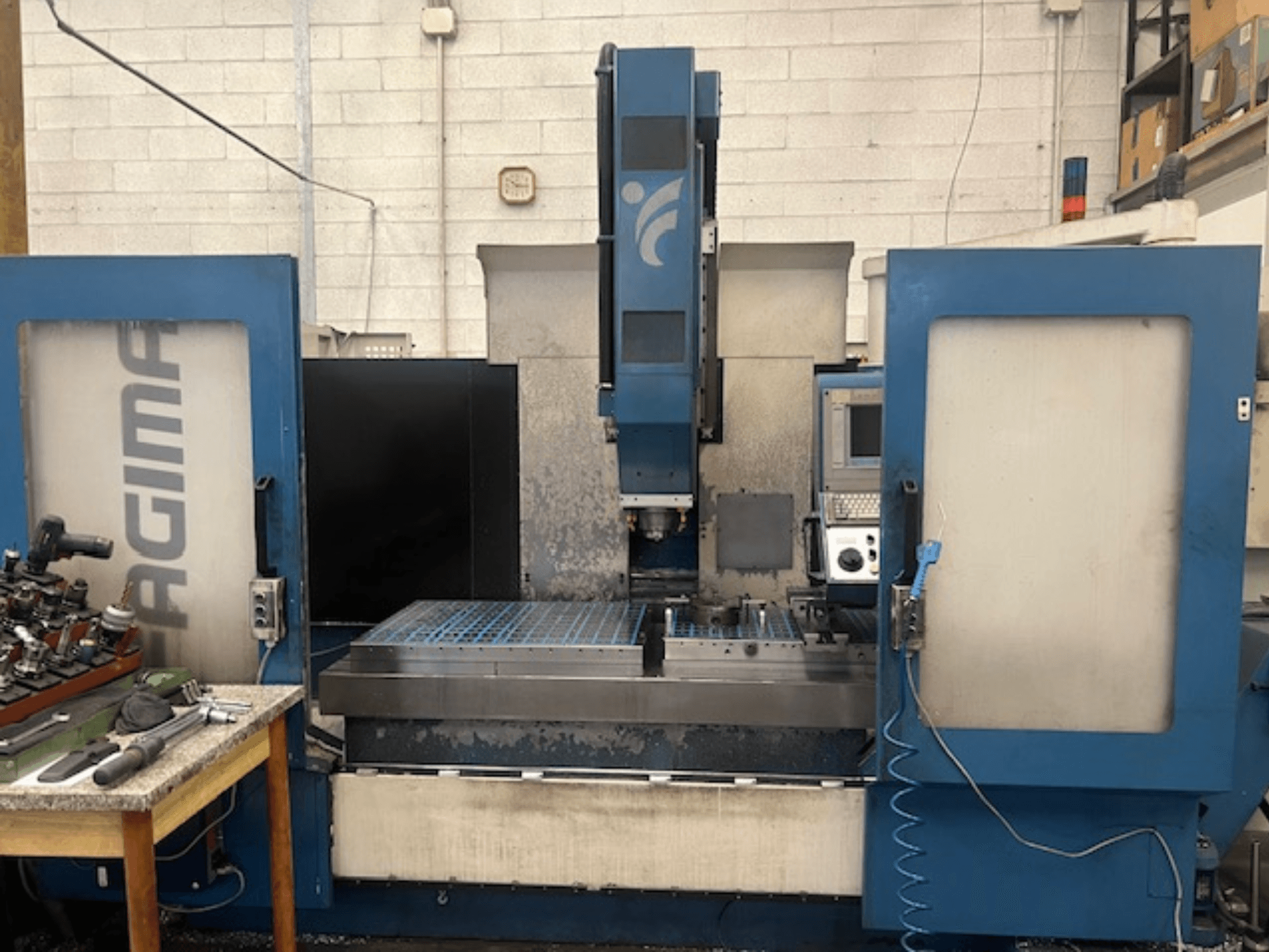 Вид спереду верстата з ЧПК JAGIMA з великою металевою робочою зоною, видимою панеллю керування та інструментами на сусідньому столі.