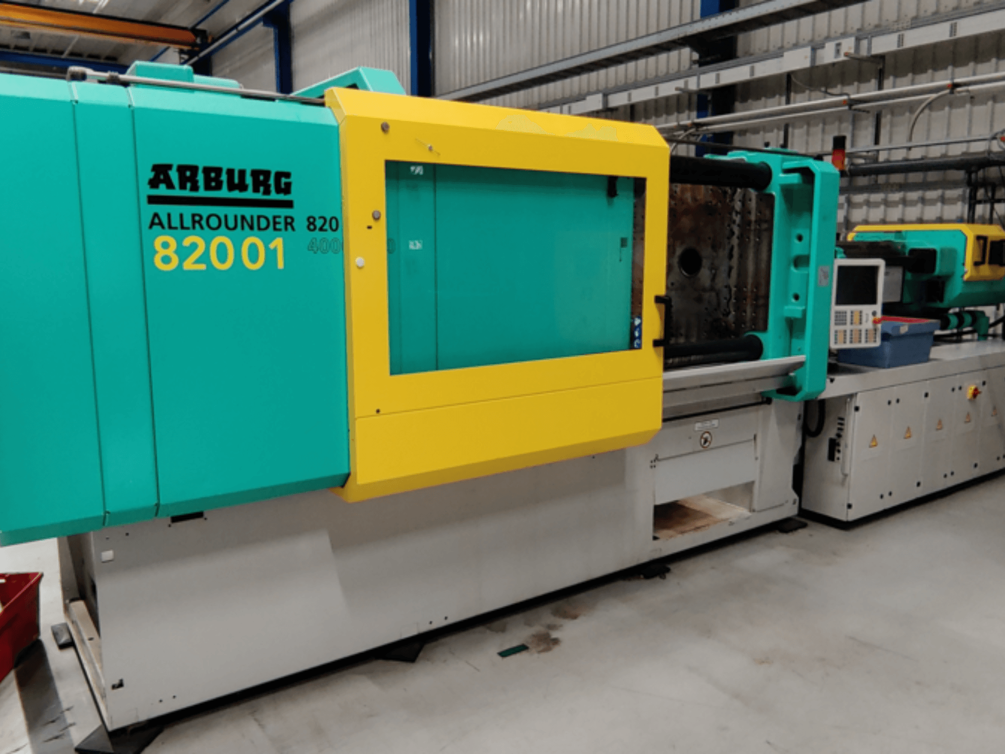 Термопластавтомат Arburg ALLROUNDER 82001 у біло-блакитному та жовтому кольорах, вид збоку з панеллю керування та робочими функціями.