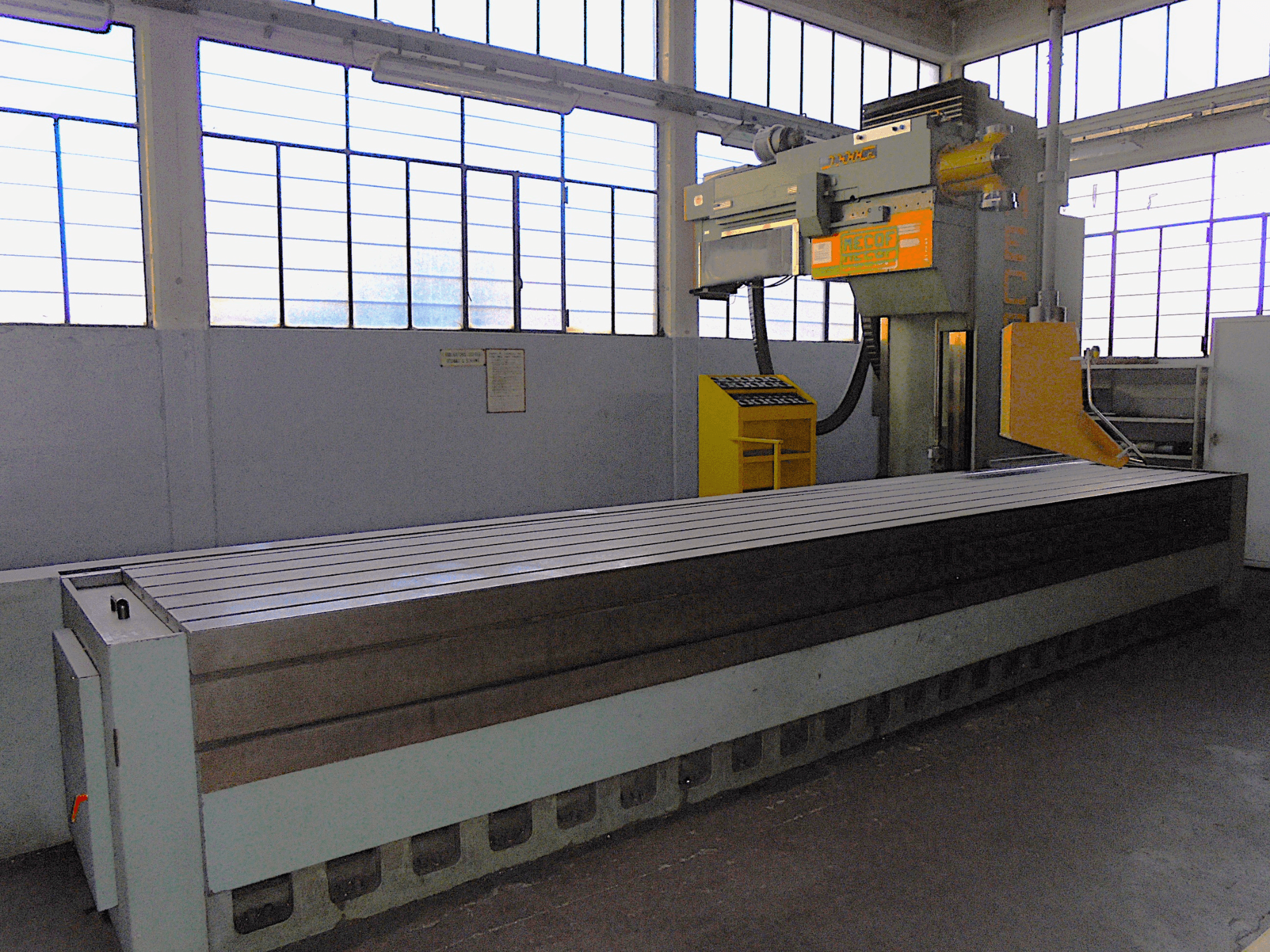 Невідома марка, вертикальний фрезерний верстат на заводі, вид збоку, має великий стіл з рифленою поверхнею та панель управління.