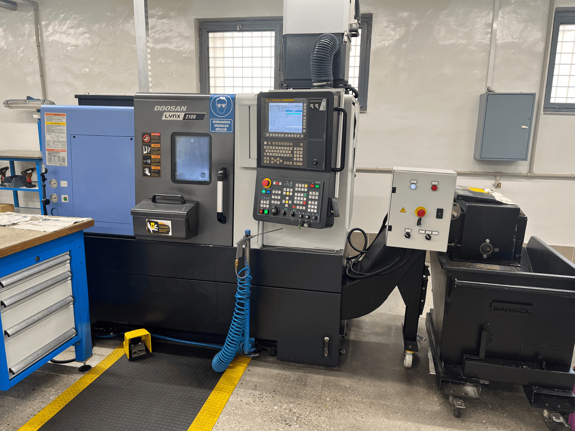 Токарний верстат Doosan Lynx 210 в майстерні: панель керування, сховище для інструментів та система охолодження, вид збоку з деталями робочого простору.
