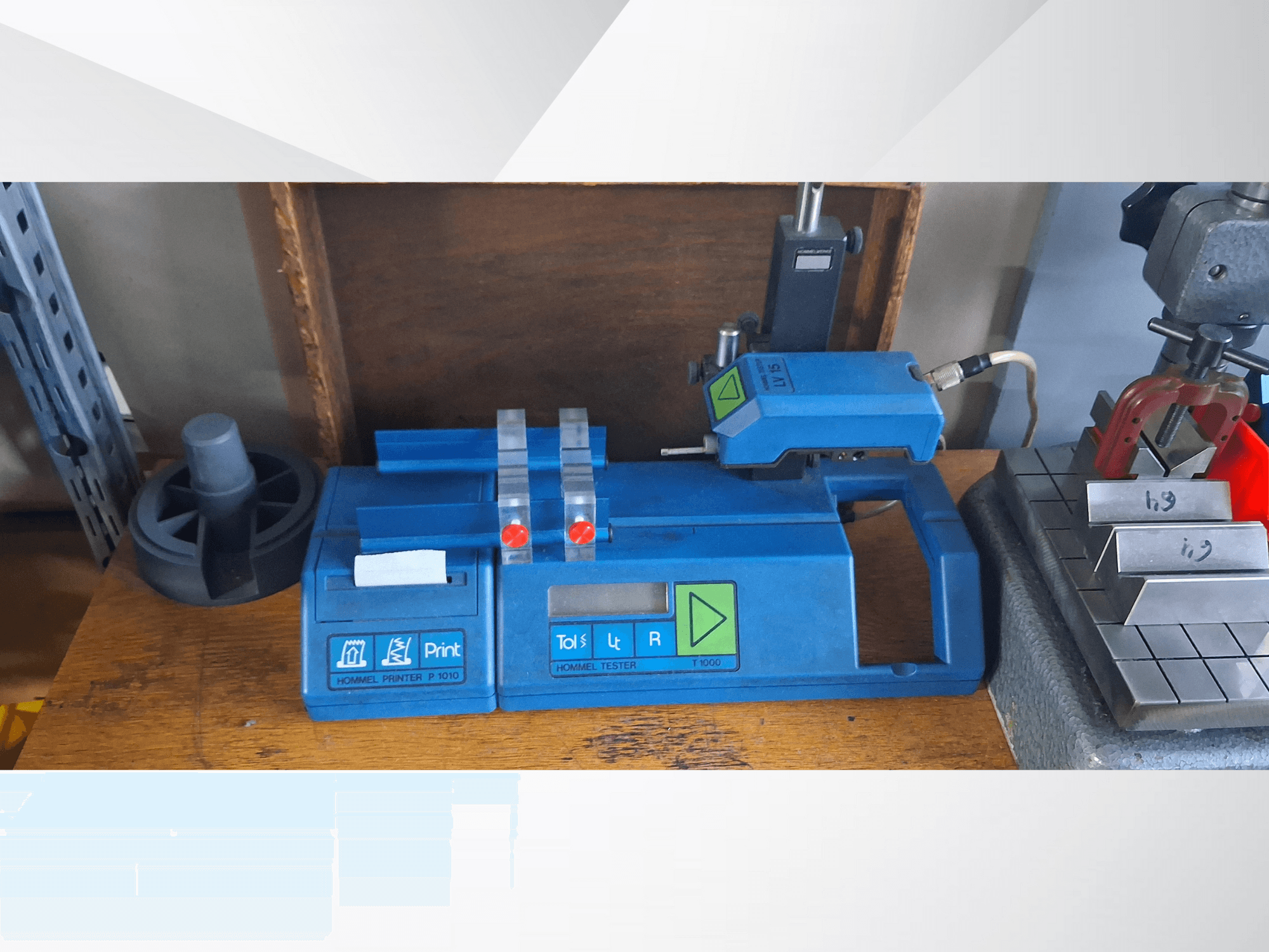 Синій принтер Hommel T 1000 і тестер T 1 010 з червоними кнопками, вигляд спереду на робочому столі з металевими блоками.