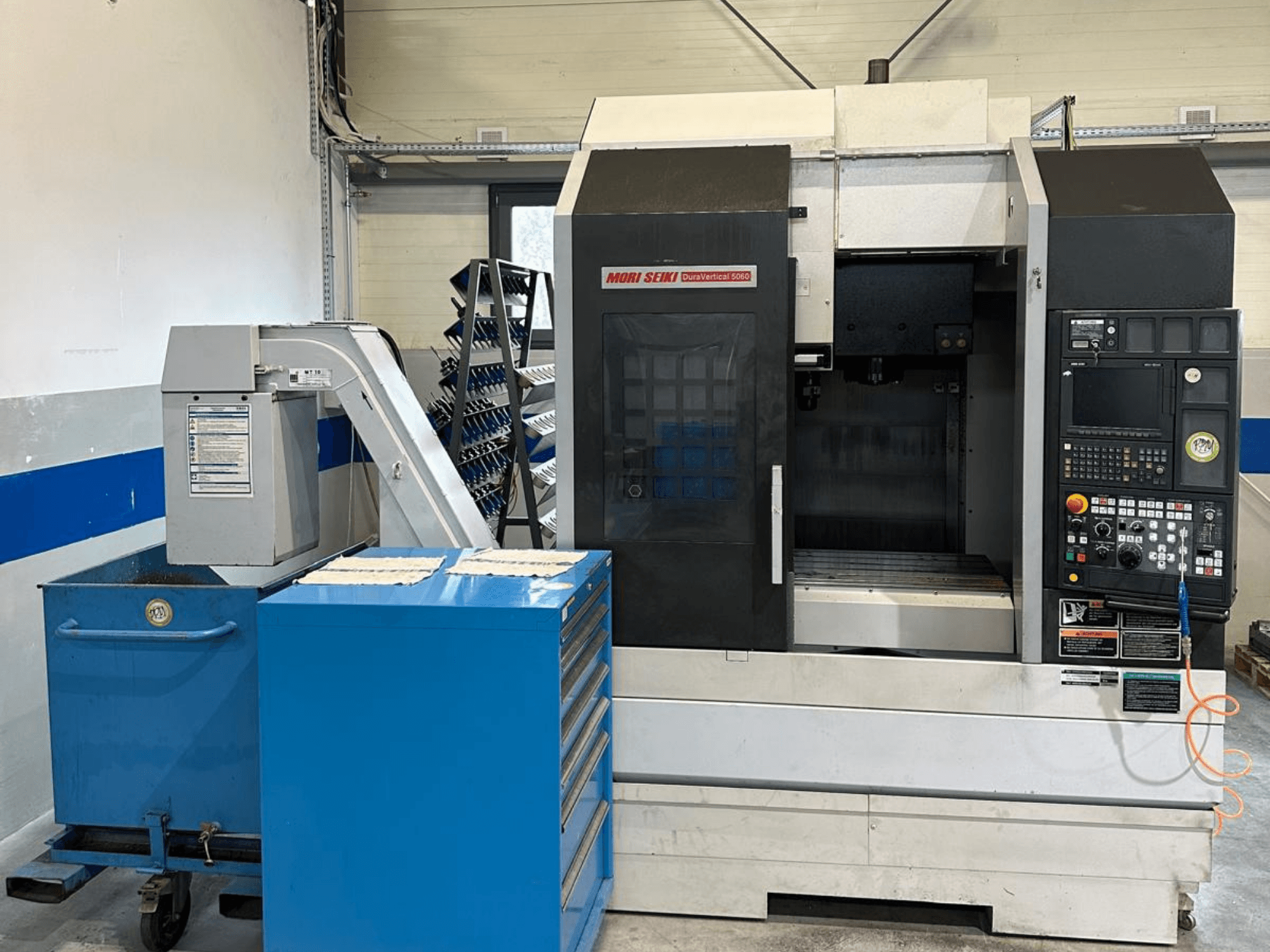MORI SEIKI DURA VERTICAL 5060 — вид спереду на вертикальний обробний центр з панеллю керування та розташованим поруч сховищем інструментів.