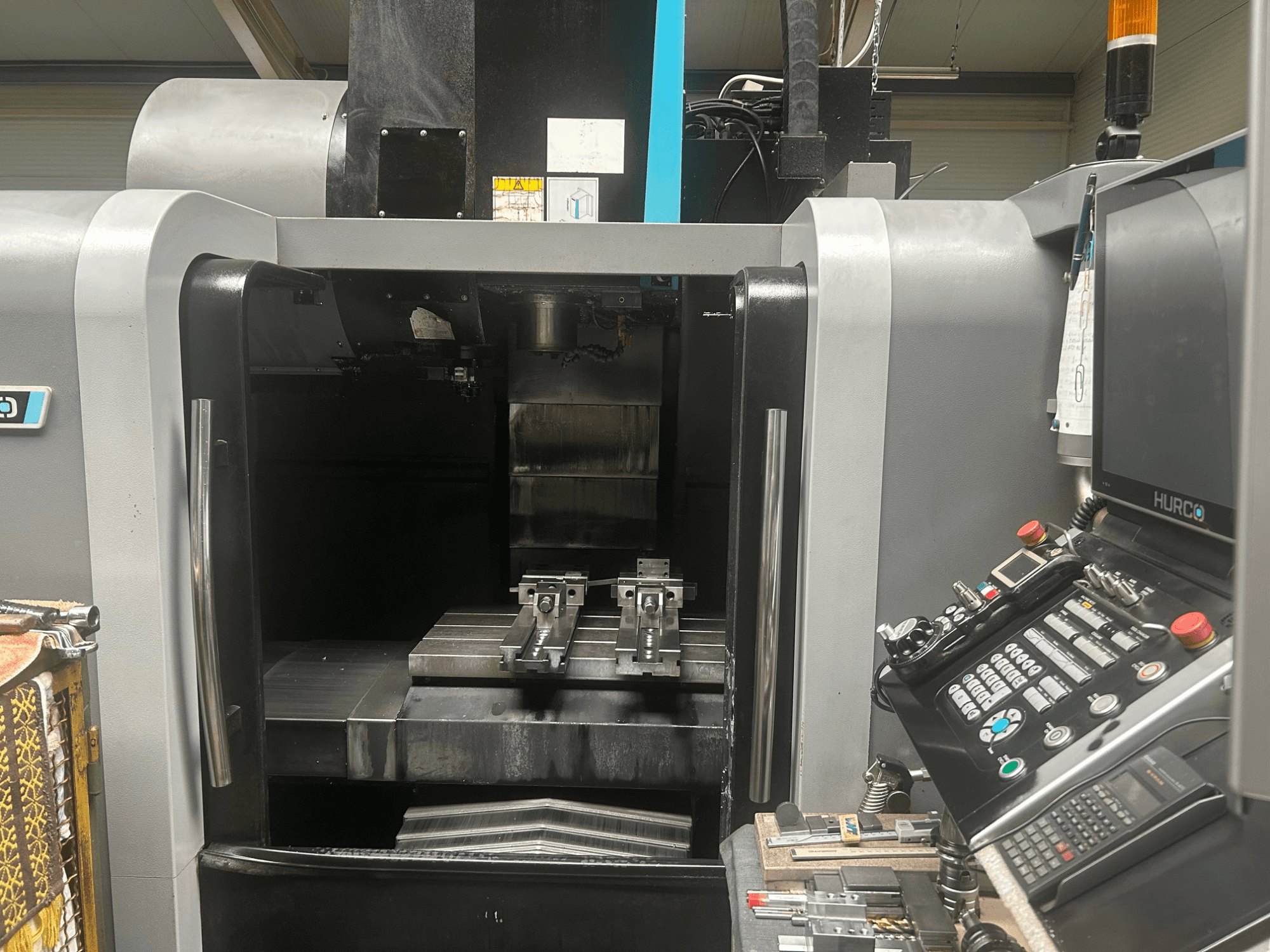 Вид спереду обробного центру з ЧПК Hurco, на якому показано тримач інструменту, металеву заготовку та панель керування з кнопками та дисплеєм.