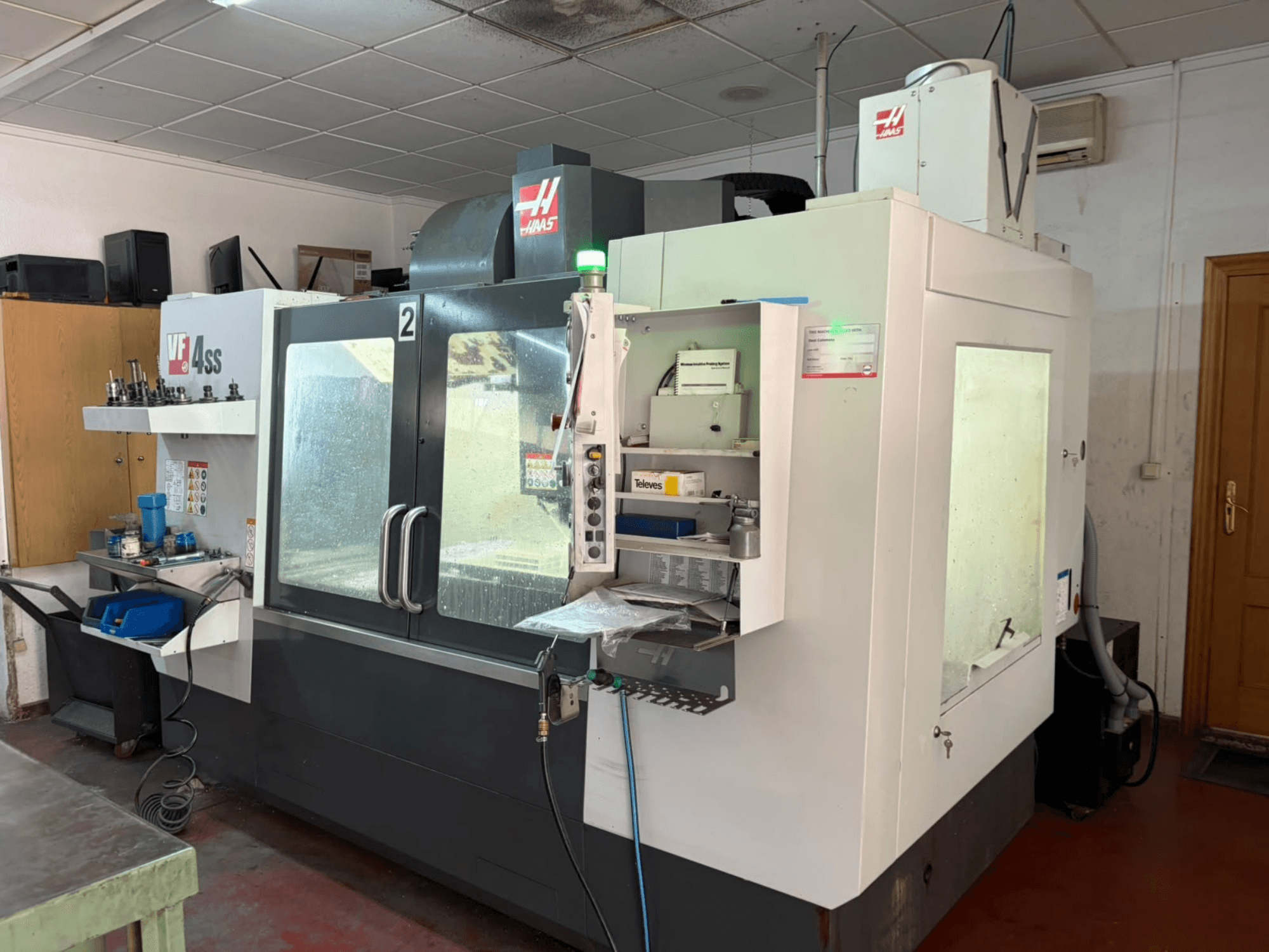 Вертикальний обробний центр HAAS VF 4SS у цеху, вид спереду, на якому видно панель управління та робочу зону з інструментами та матеріалами.