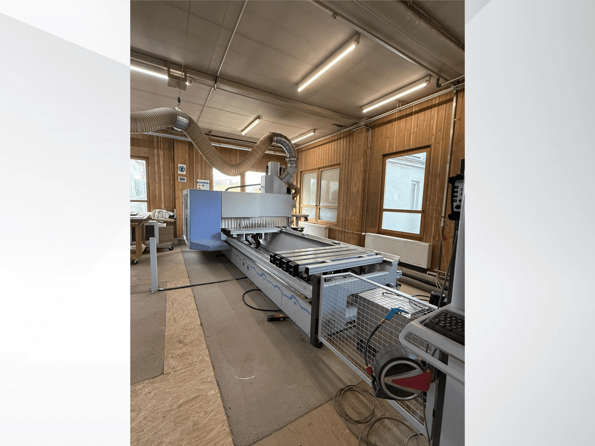 Фрезерний верстат з ЧПУ в майстерні, вид збоку, з великим синім корпусом, прикріпленим стрічковим конвеєром і видимою панеллю керування.