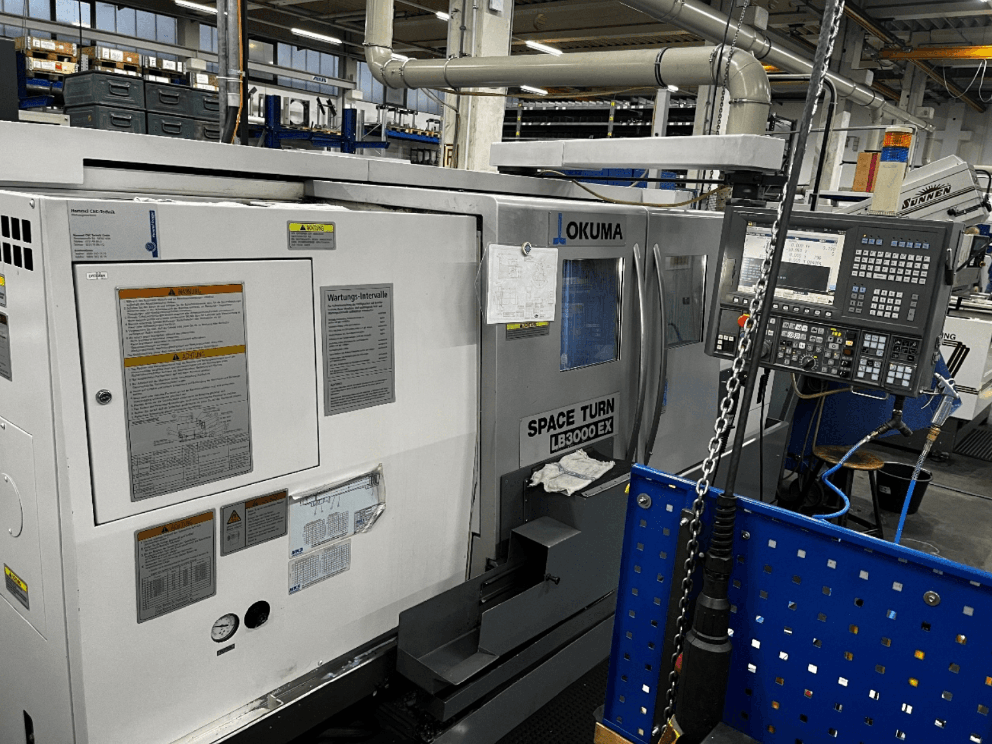Горизонтальний токарний верстат Okuma LB3000 EX, вид спереду, панель керування та інформація з техніки безпеки збоку.