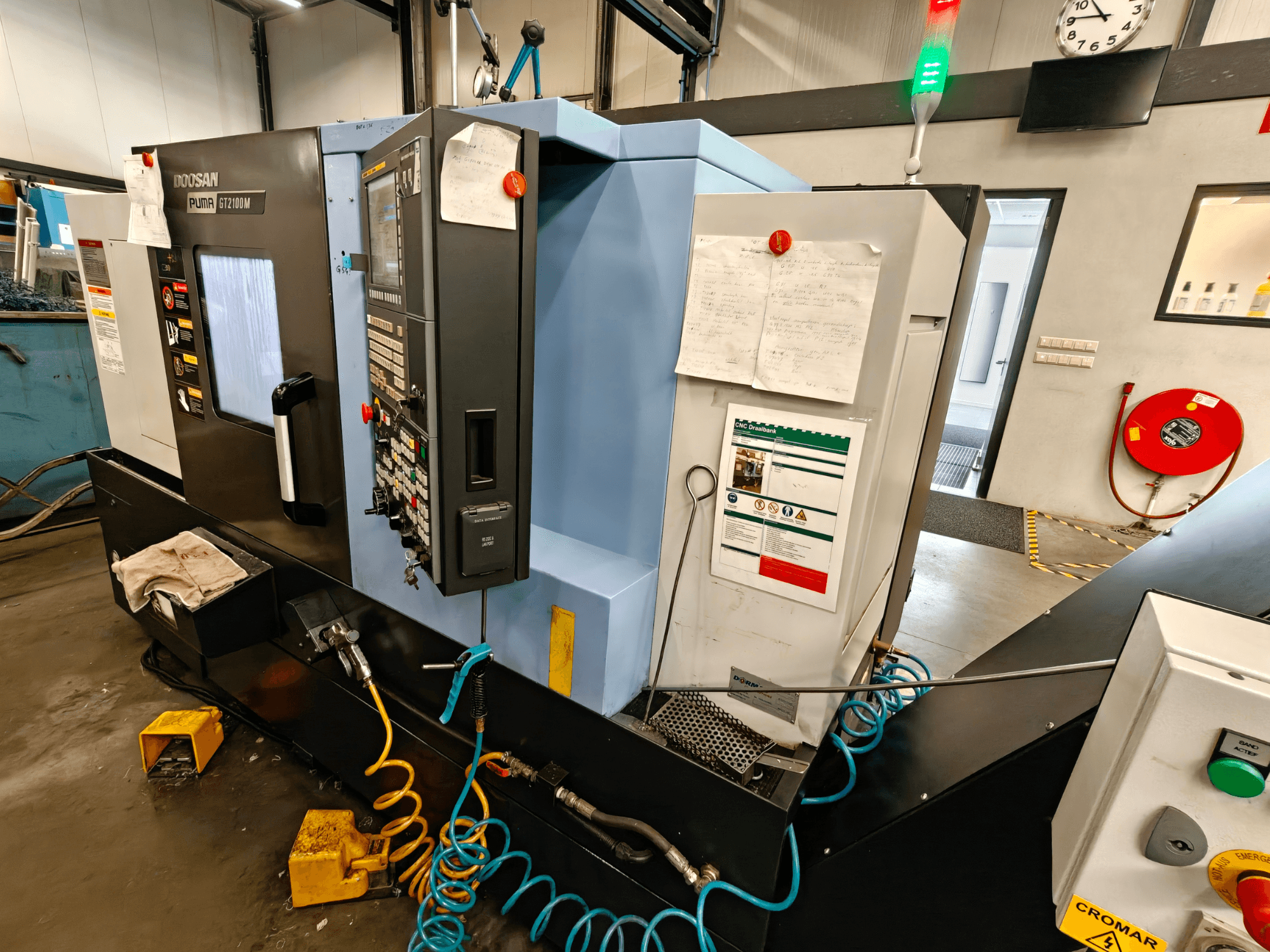 Вид спереду горизонтального токарного верстата DOOSAN Puma GT 2100M з панеллю керування, елементами безпеки та інструкціями з технічного обслуговування.