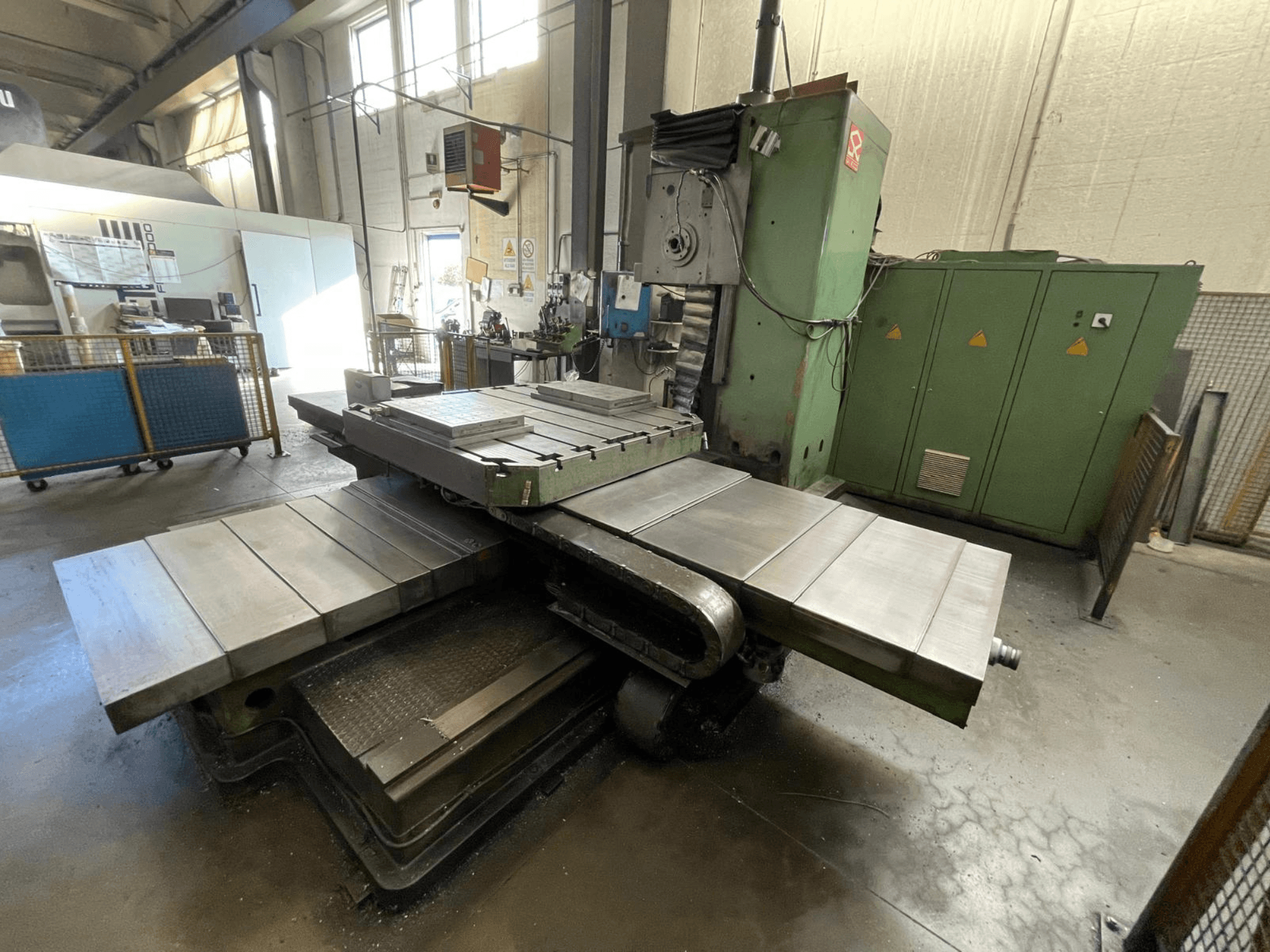 Великий промисловий фрезерний верстат із зеленим корпусом, вид збоку, з декількома плоскими поверхнями та шафами для зберігання на задньому плані.