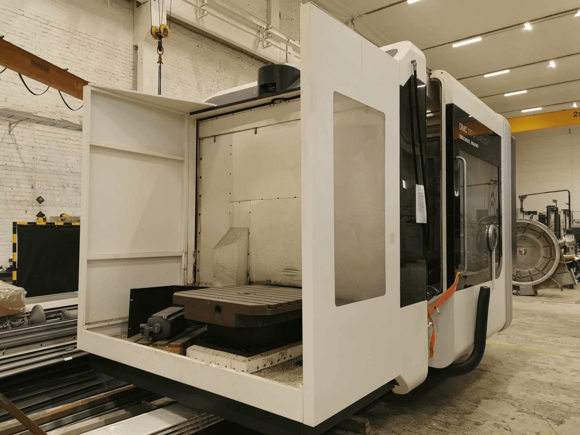 Лінійний верстат з ЧПК DMC 100U, вид збоку з відкритими дверцятами, показує робочий стіл і внутрішні компоненти.