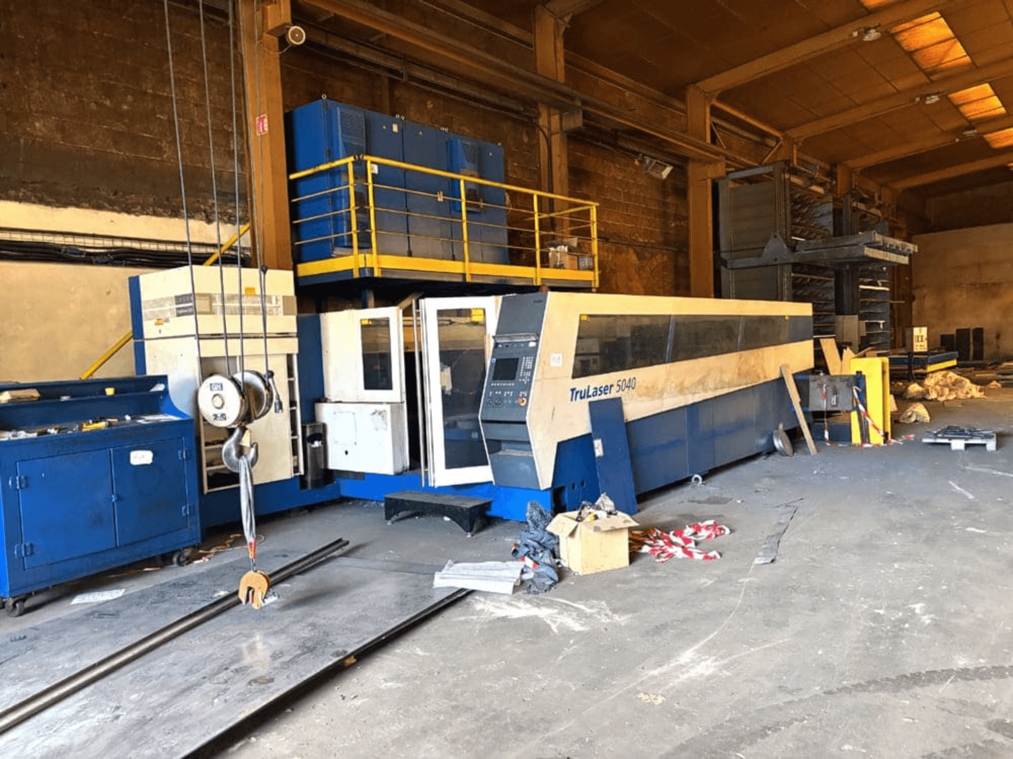 Лазерний верстат для різання CO2 від компанії TRUMPF, модель TRULASER 5040, зображений у цеху; похилий вид спереду на захаращеному тлі.