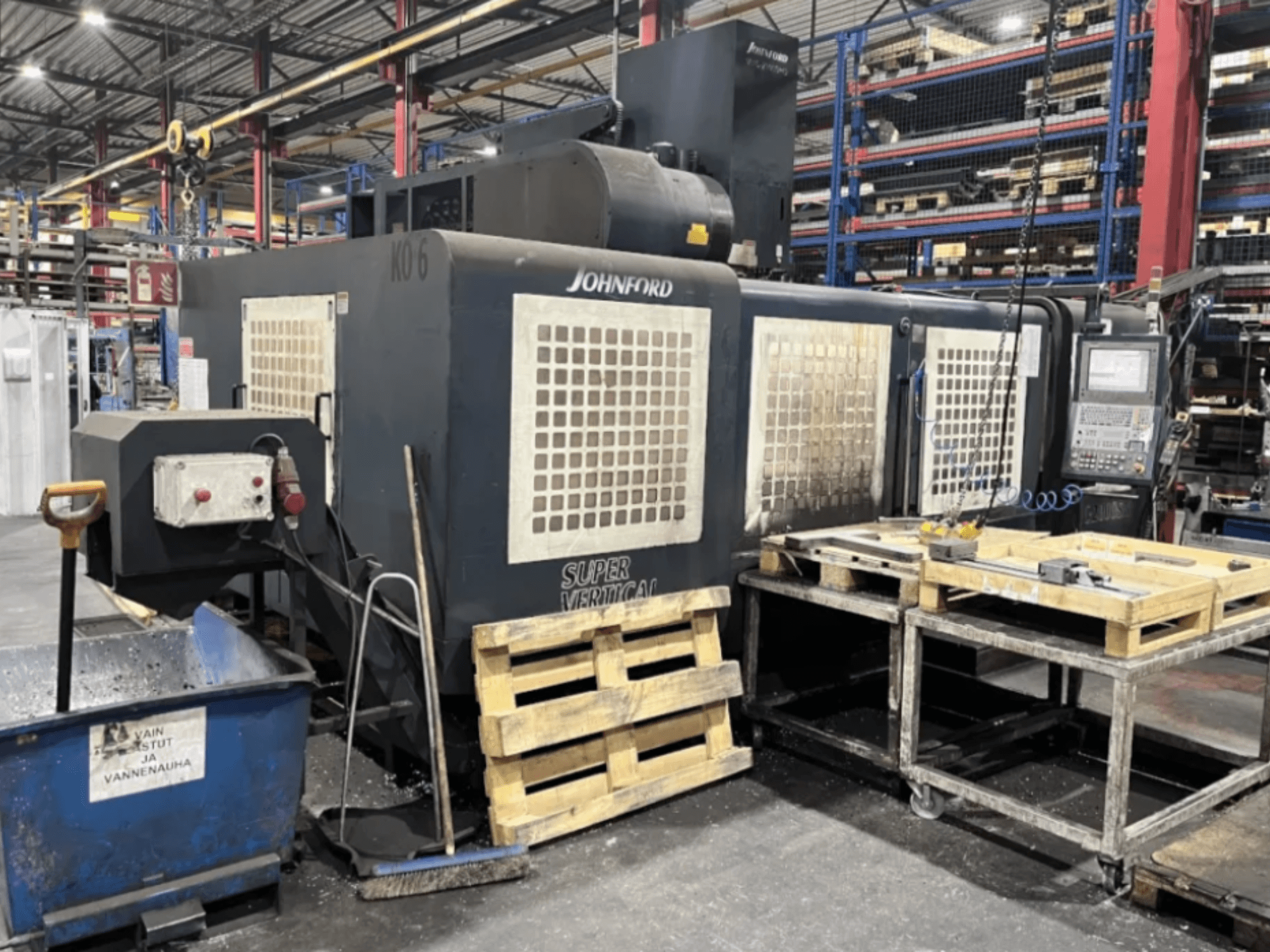 Фрезерний верстат Johnford Super Vertical на заводі, вид збоку з панеллю керування, піддонами та очисним обладнанням поруч.