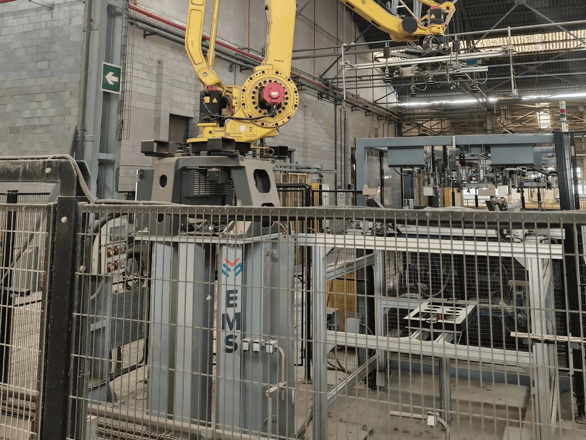 Вигляд спереду на маніпулятор робота FANUC M-410iC/315, розташований над інструментом для поверхневого монтажу (EMS), на тлі якого видно промислове обладнання та огорожу.