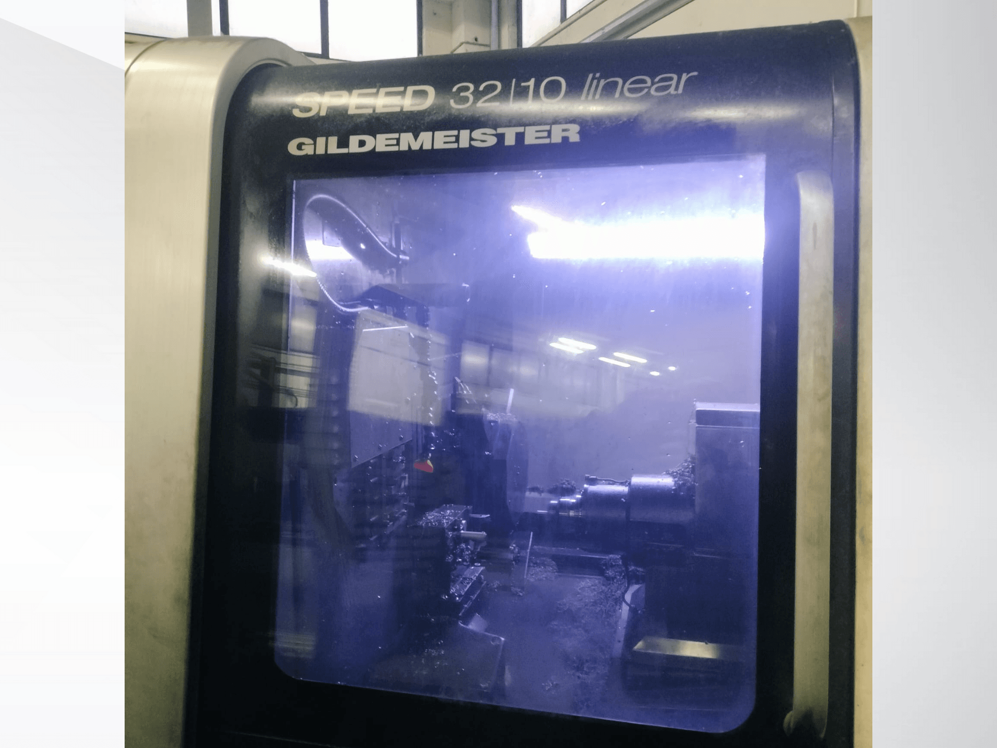 Лінійний верстат з ЧПК Gildemeister SPEED 3210, вигляд спереду, показані внутрішні компоненти та рідка охолоджуюча рідина в роботі.