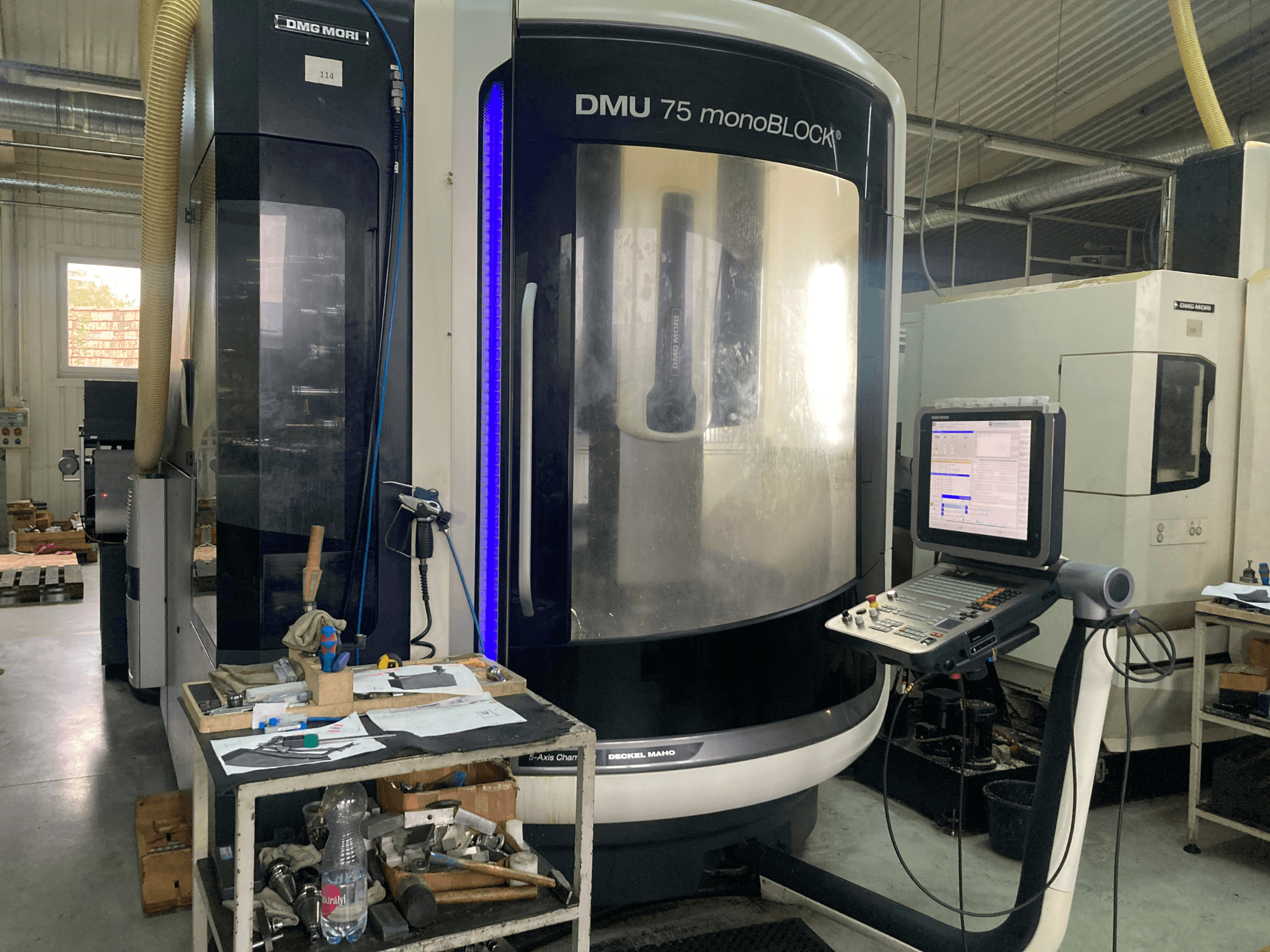 Верстат з ЧПК DMG MORI DMU 75 monoBLOCK®, вид спереду, з панеллю керування, інструментами та робочою зоною з матеріалами.
