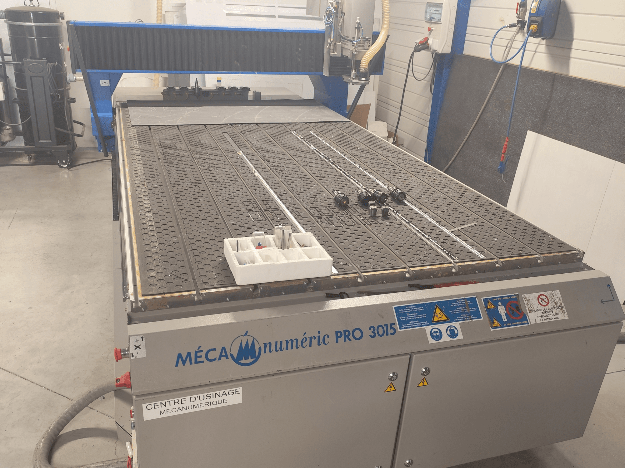 Фрезерний верстат з ЧПУ MECANUMERIC Pro 3015 у фронтальному ракурсі: на фото видно робочий стіл з детальним зображенням, панель керування та аксесуари, розташовані на столі.