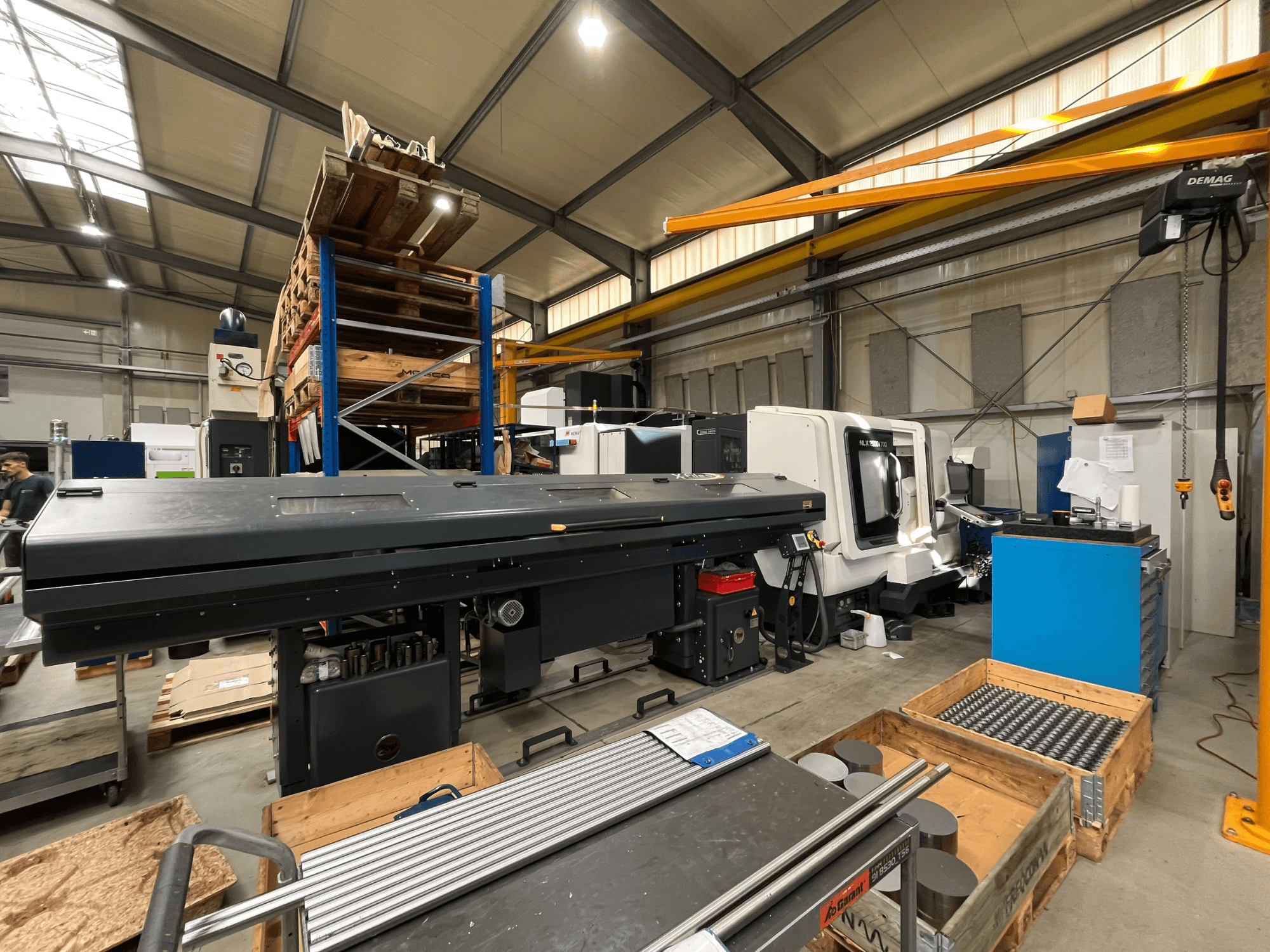 Горизонтальний токарний верстат DMG MORI MORI NLX 2500/700 SY у цеху, вид збоку, на задньому плані — складські приміщення та інструменти.