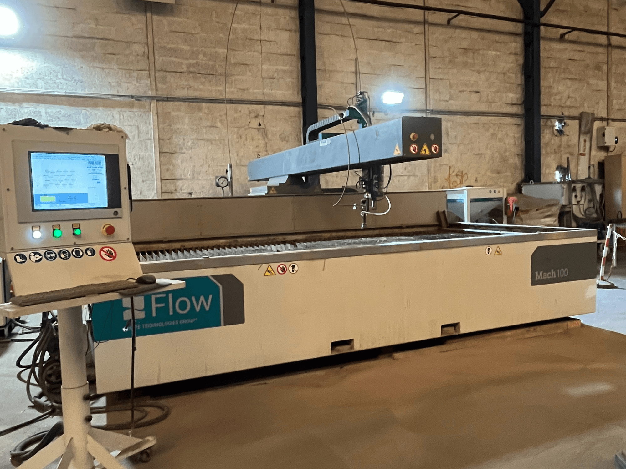 Гідроабразивний різак Flow Mach 100, вид збоку, з цифровою панеллю керування і ріжучою головкою, видимою на робочому столі.
