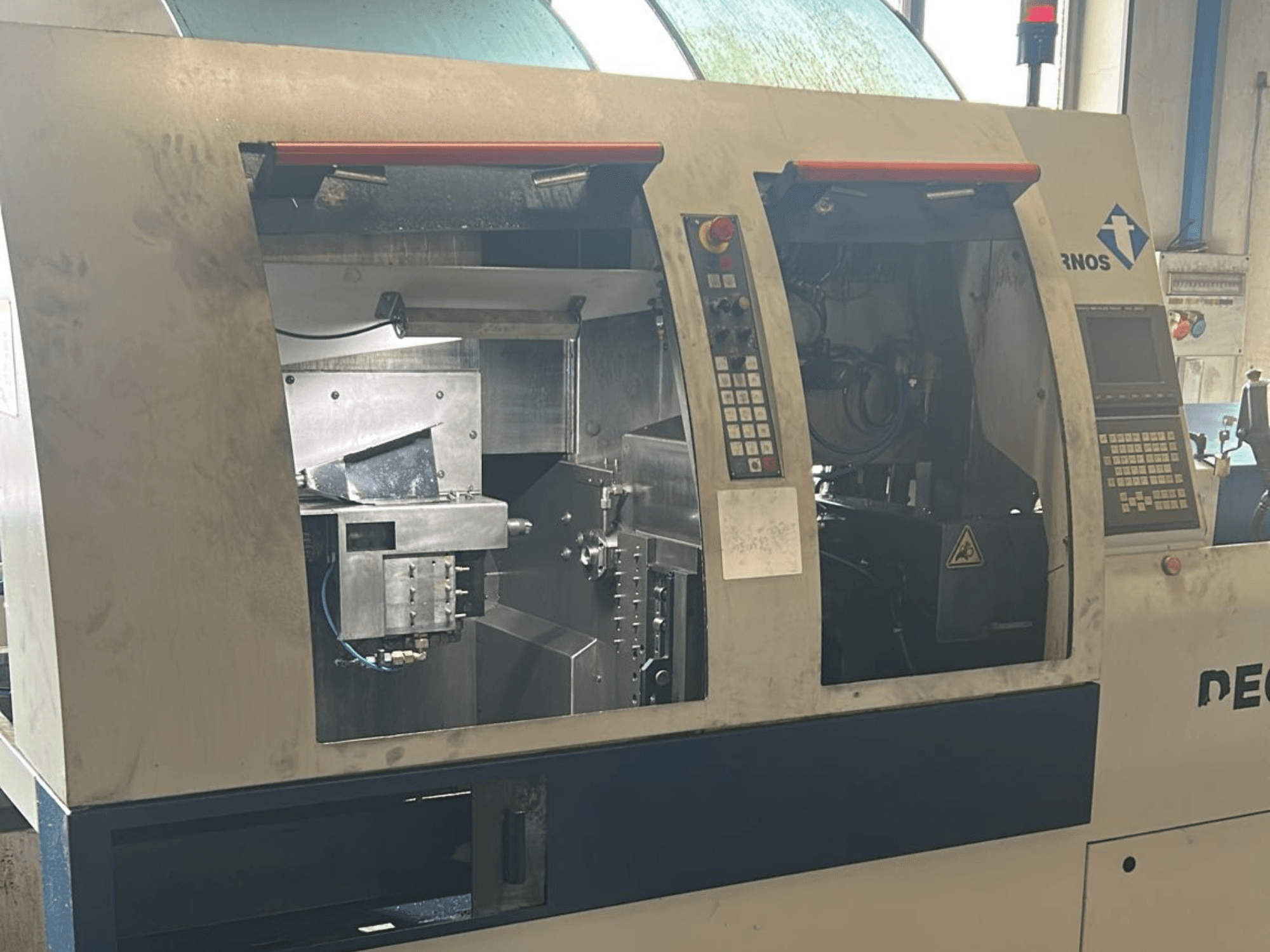 Альтернативний текст: Токарний верстат швейцарського типу TORNOS Deco 13 b спереду з панелями керування та внутрішніми компонентами.