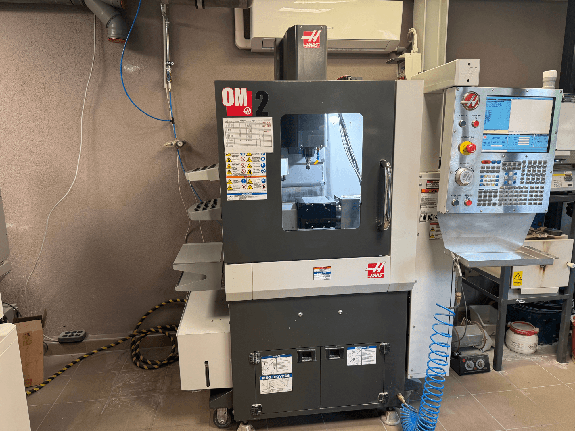 Верстат з ЧПК Haas OM-2, вид спереду, з панеллю керування, шпинделем та етикетками безпеки, встановлений в умовах майстерні.