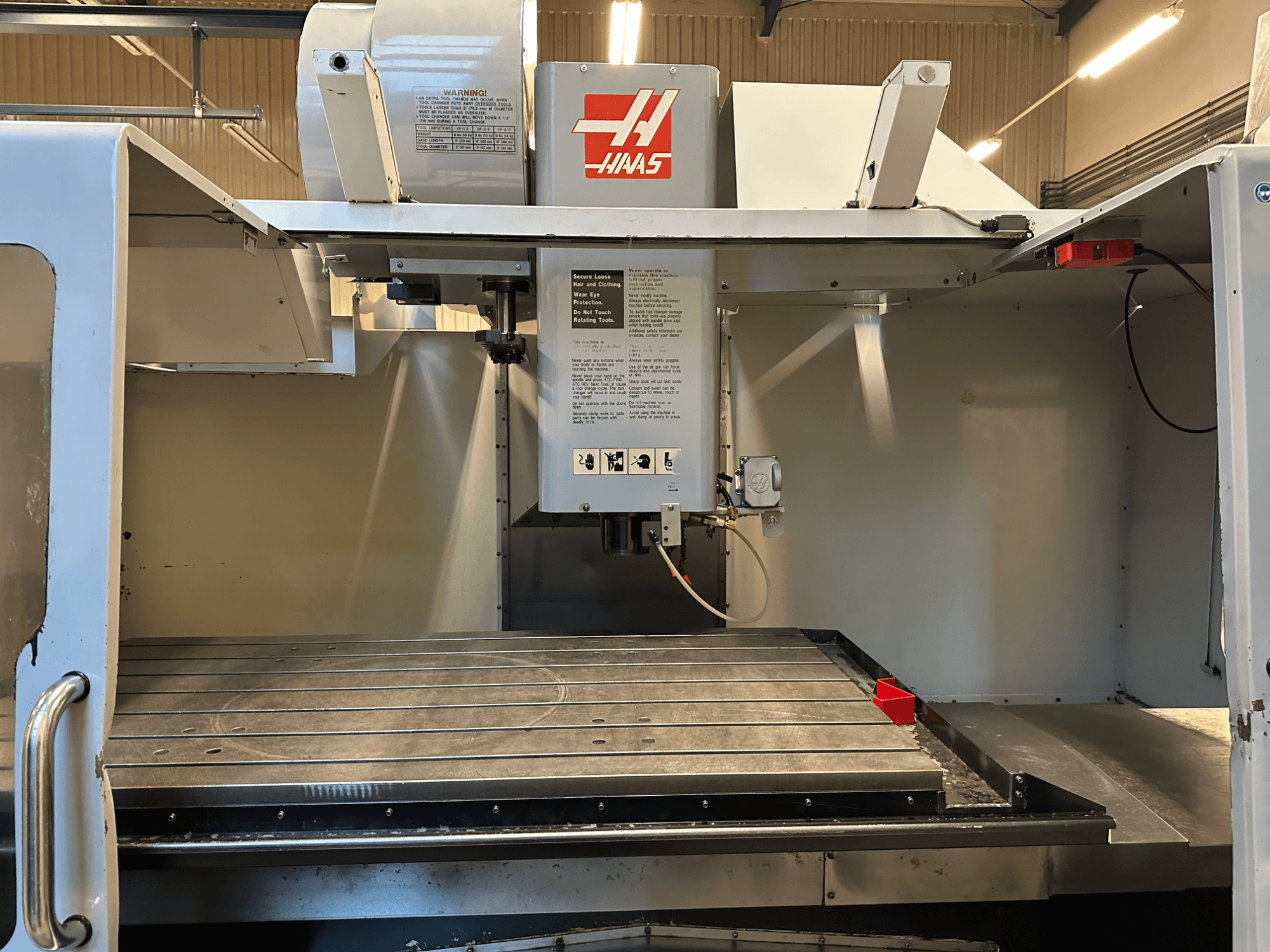 Фрезерний верстат з ЧПК Haas, модель VF-2, вид спереду з елементами керування, робочим столом та етикеткою безпеки на панелі.