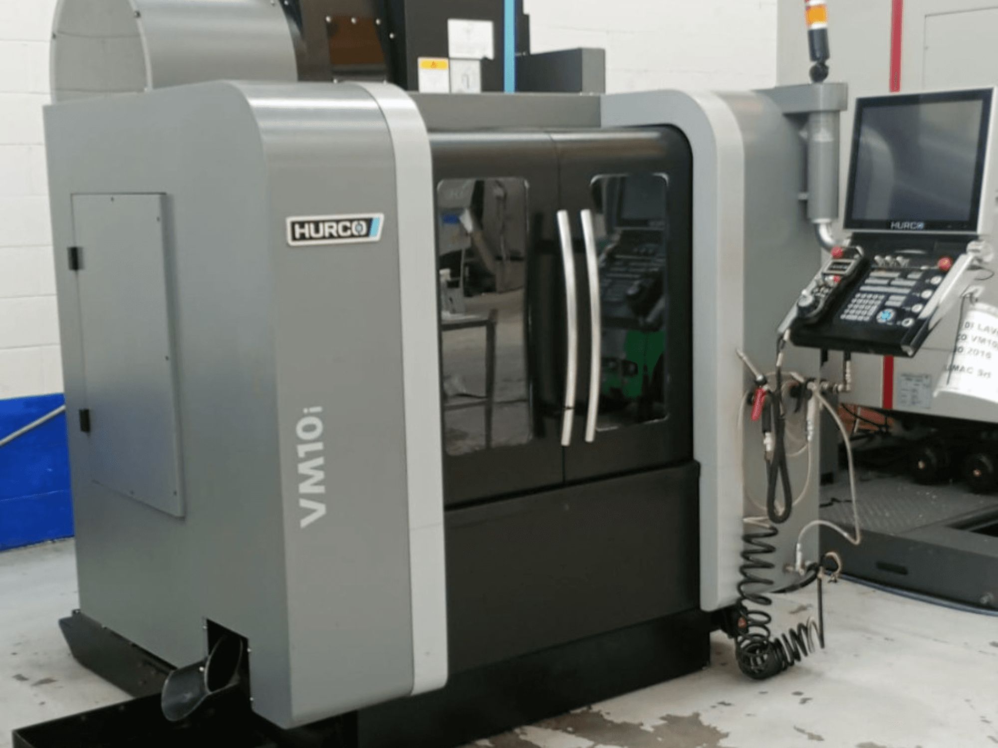 Вертикальний обробний центр Hurco VM10i у боковому ракурсі: з подвійними дверцятами, панеллю керування та кабелями, необхідними для роботи.