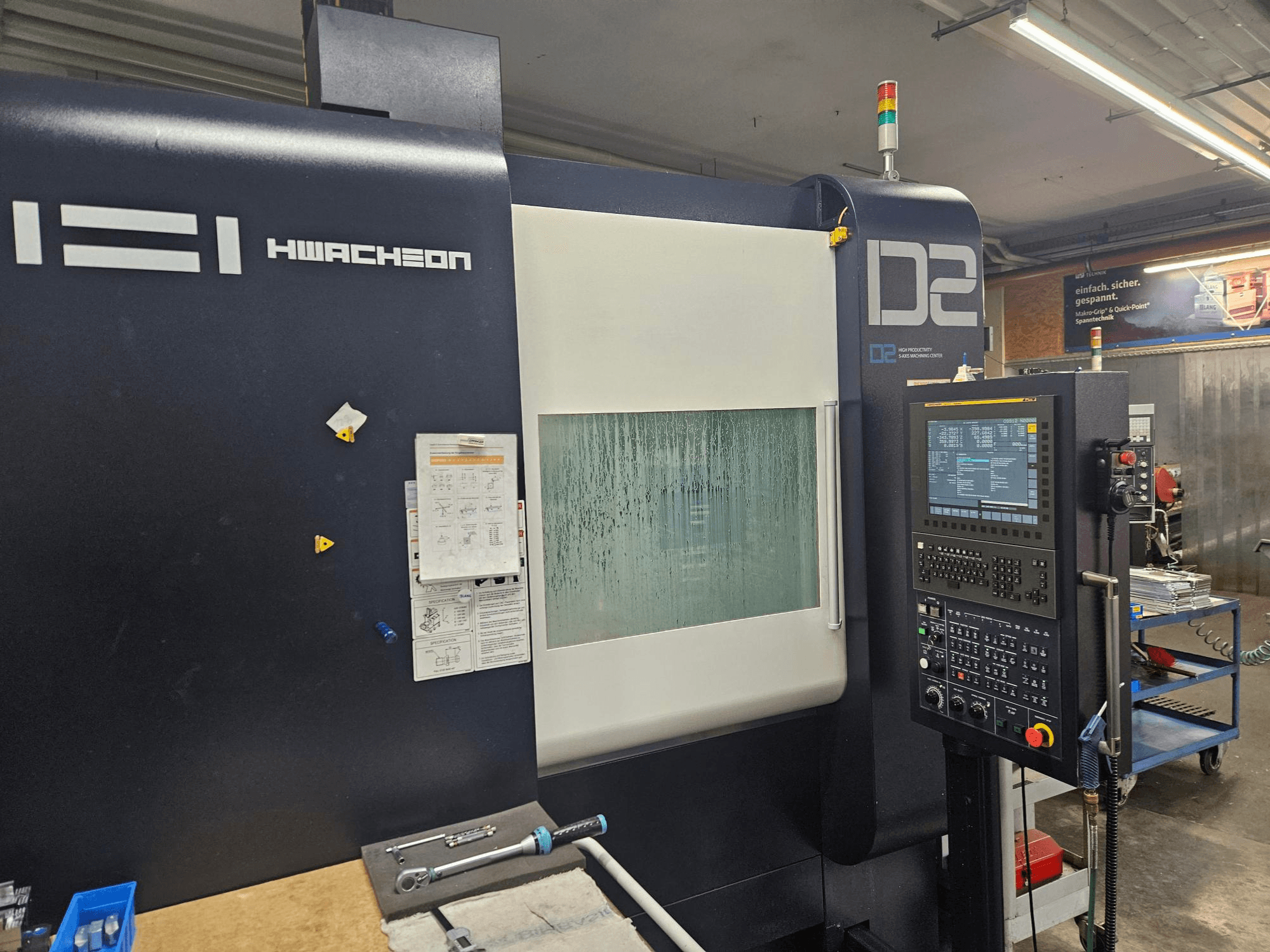 Вертикальний обробний центр HWACHEON D2-5AX 12k, вид спереду, на якому видно панель керування та запітніле оглядове вікно.