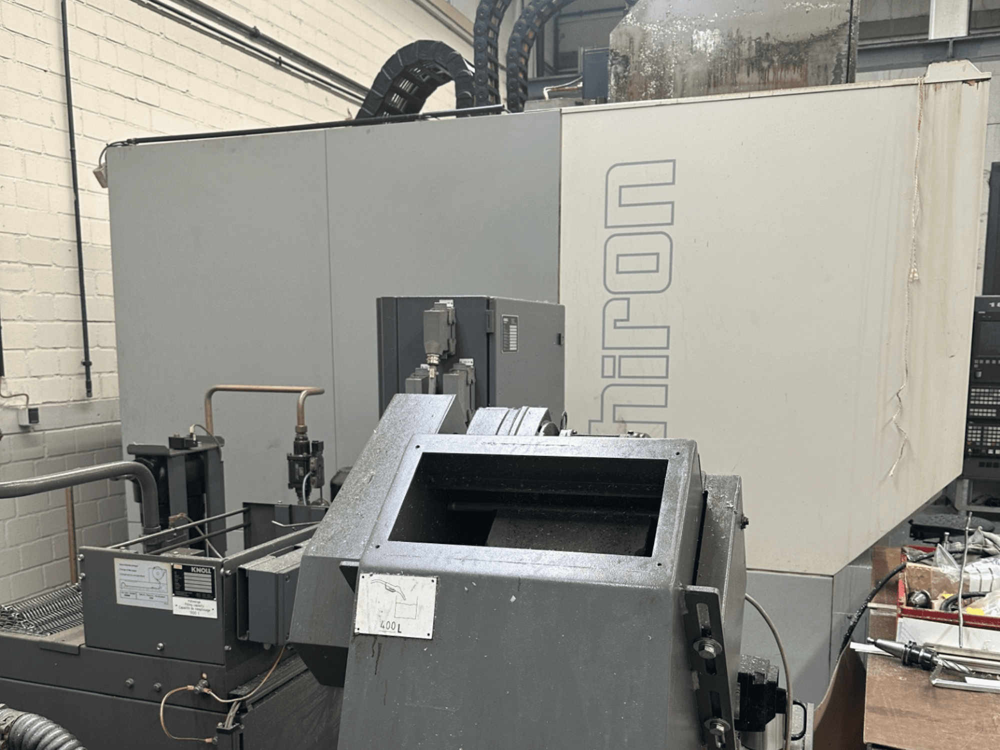 БРЕНД: Chiron; вигляд спереду промислового верстата з ЧПК із сірим зовнішнім виглядом, видимою панеллю керування та компонентами машини у фокусі.