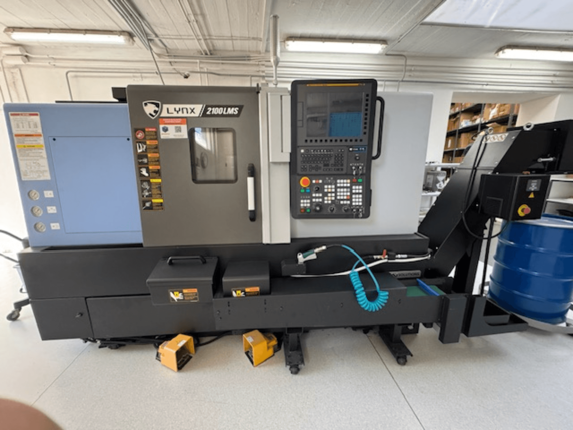 Горизонтальний токарний верстат DOOSAN LYNX 2100LMSA, вид спереду, з панеллю керування, шлангом для охолоджувальної рідини та ящиками для зберігання.