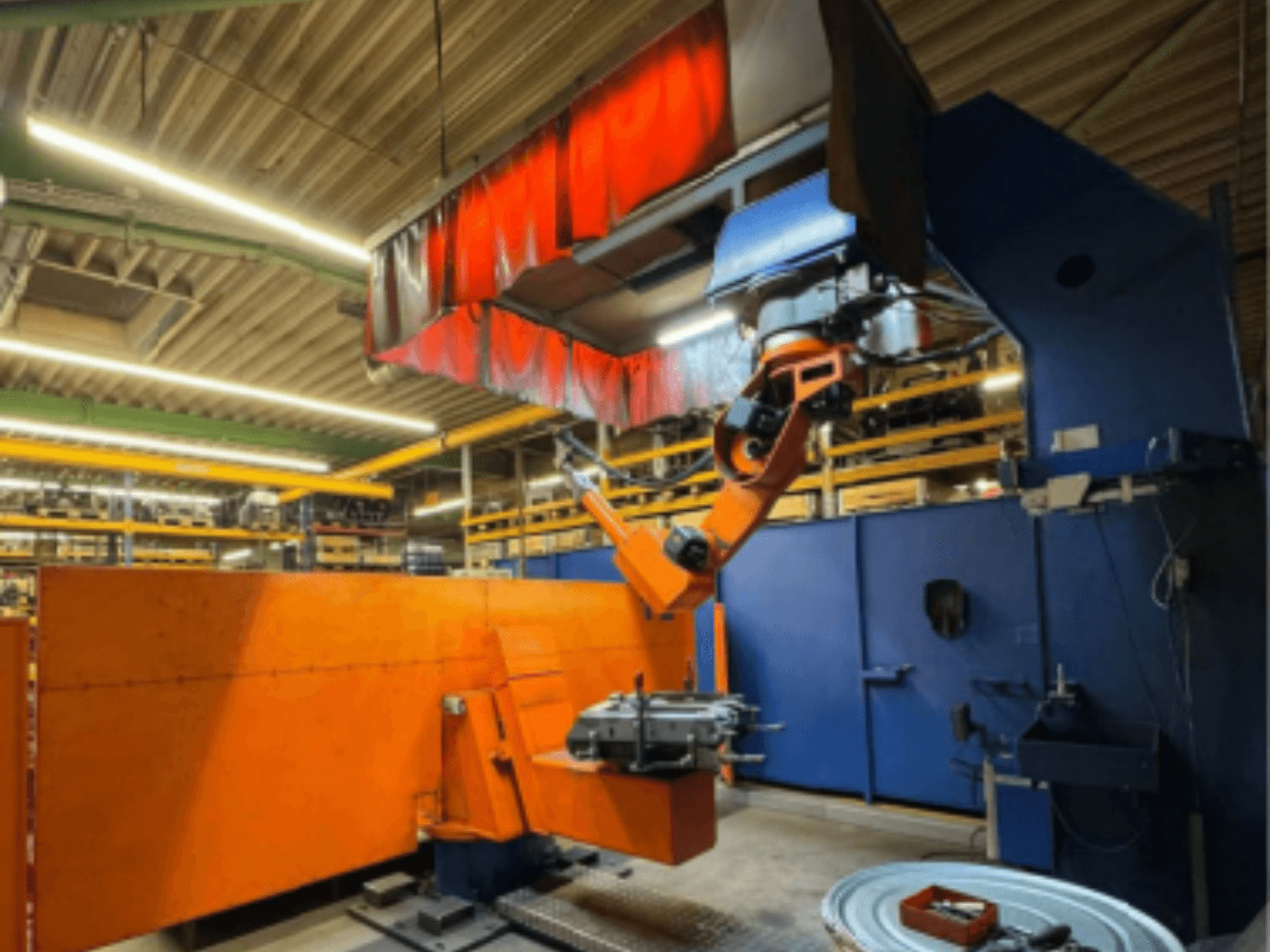 Зварювальний робот CLOOS Romat 350 e в промислових умовах, вид спереду з помаранчевою рукою, що тримає заготовку під верхньою шторкою.