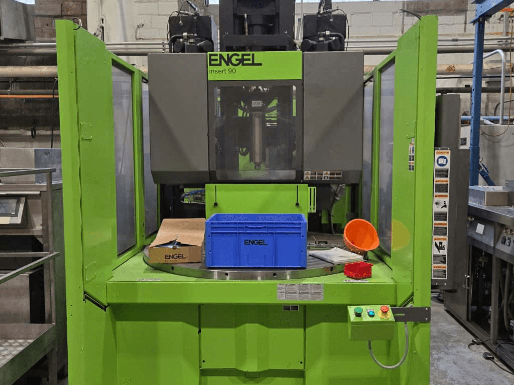 Зелена термопластавтомат ENGEL Insert 90, вид спереду, з синім контейнером і панеллю керування з кнопками.