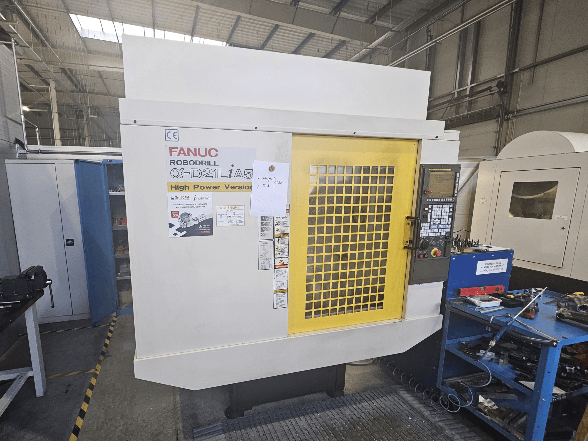 Вид спереду на робот-дриль FANUC α-D21LiA5 із жовтими захисними дверцятами, панеллю керування та інструментами на робочому місці.