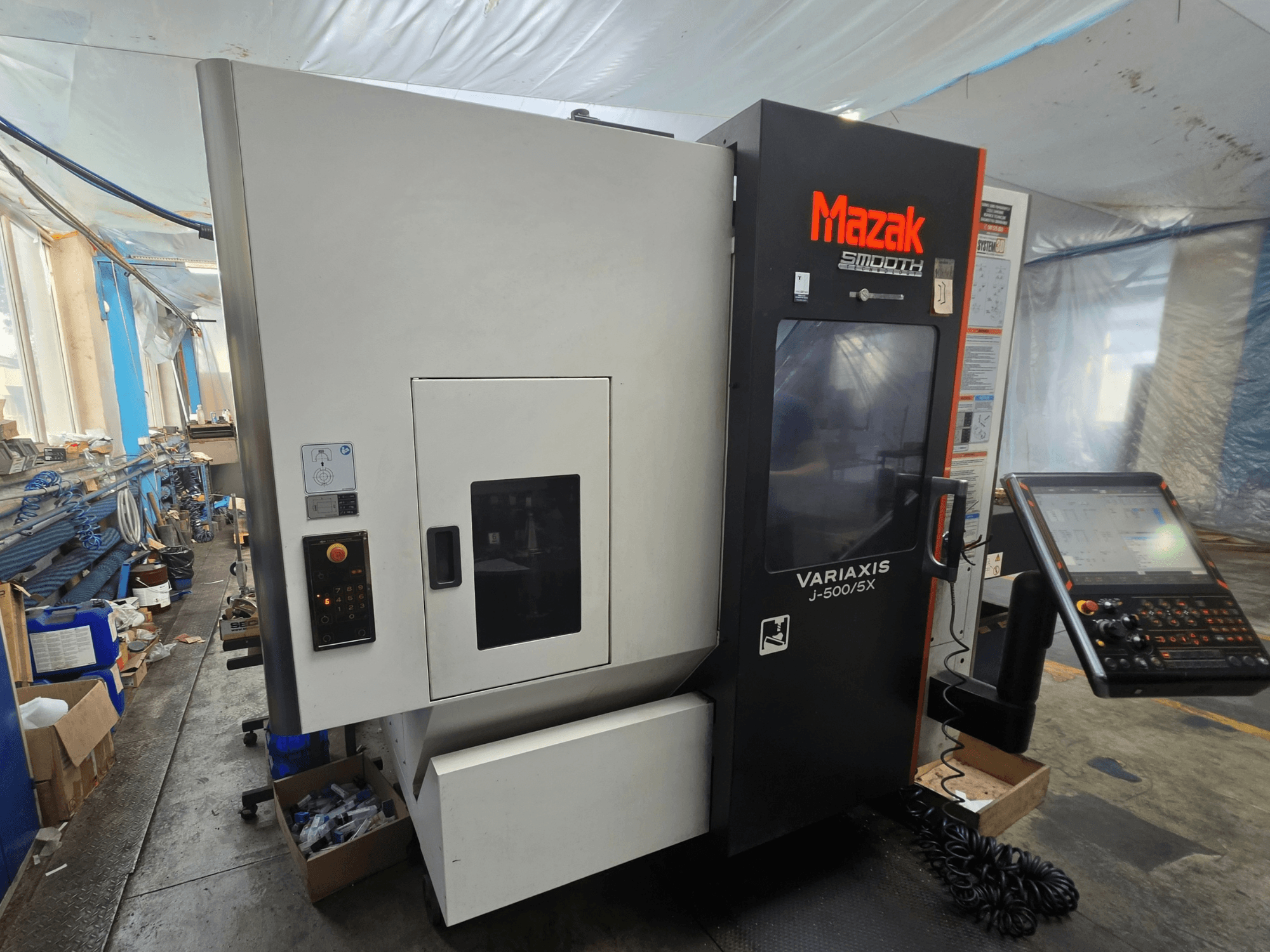 Вертикальний обробний центр Mazak VARIAXIS J-500/5X, вид збоку, на якому видно органи управління та дисплей, встановлений у цехових умовах.