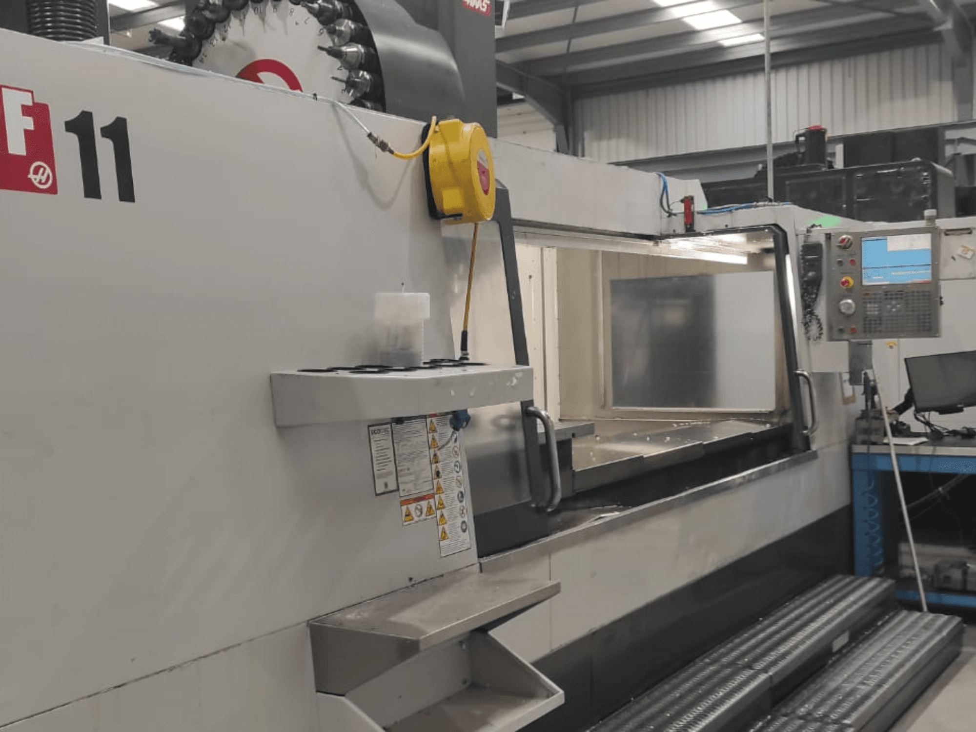Машина Haas, модель VF-11, показана спереду з панеллю керування, великою робочою зоною та етикетками безпеки.