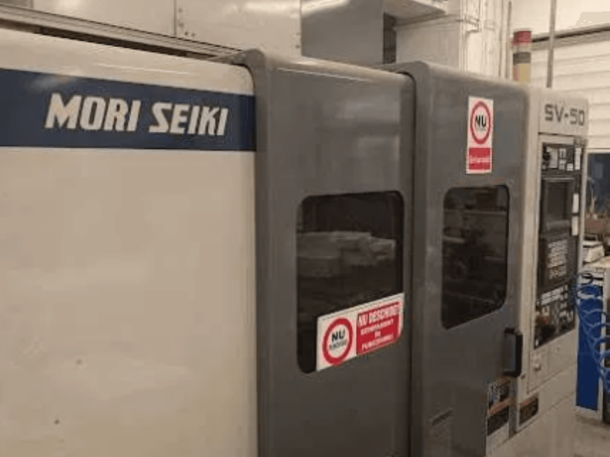 Верстат з ЧПК MORI SEIKI SV-50, вид збоку; з панеллю керування та попереджувальними наклейками про безпеку.