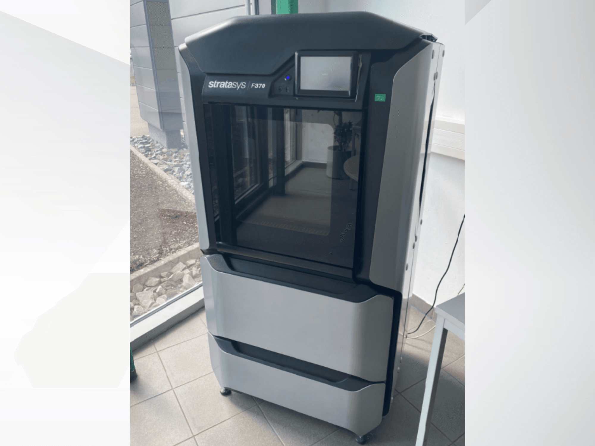 Пластиковий 3D-принтер Stratasys F370, вигляд спереду, демонструє елегантний чорно-сірий дизайн із сенсорним дисплеєм.